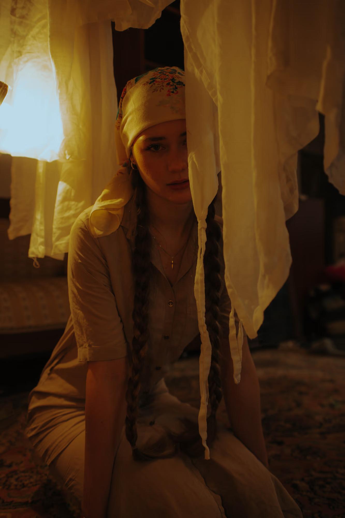 Full body fashion art shot of woman in white traditional outfit standing in dark interior with candle light on floor, dramatic vertical composition, ethno art editorial