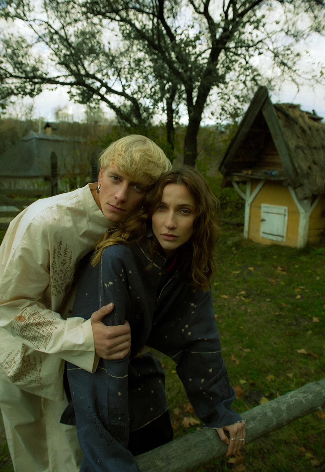 Contemporary fashion editorial featuring models in neutral wool tones against the rustic fences of the Pirogovo folk museum.