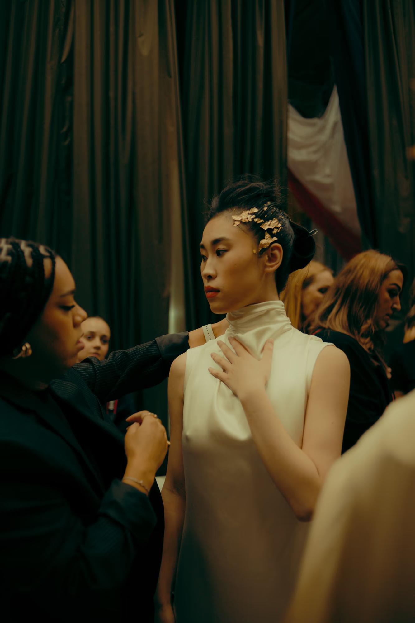 Stylists and hair professionals working on models in a busy backstage environment, high-fashion runway prep.