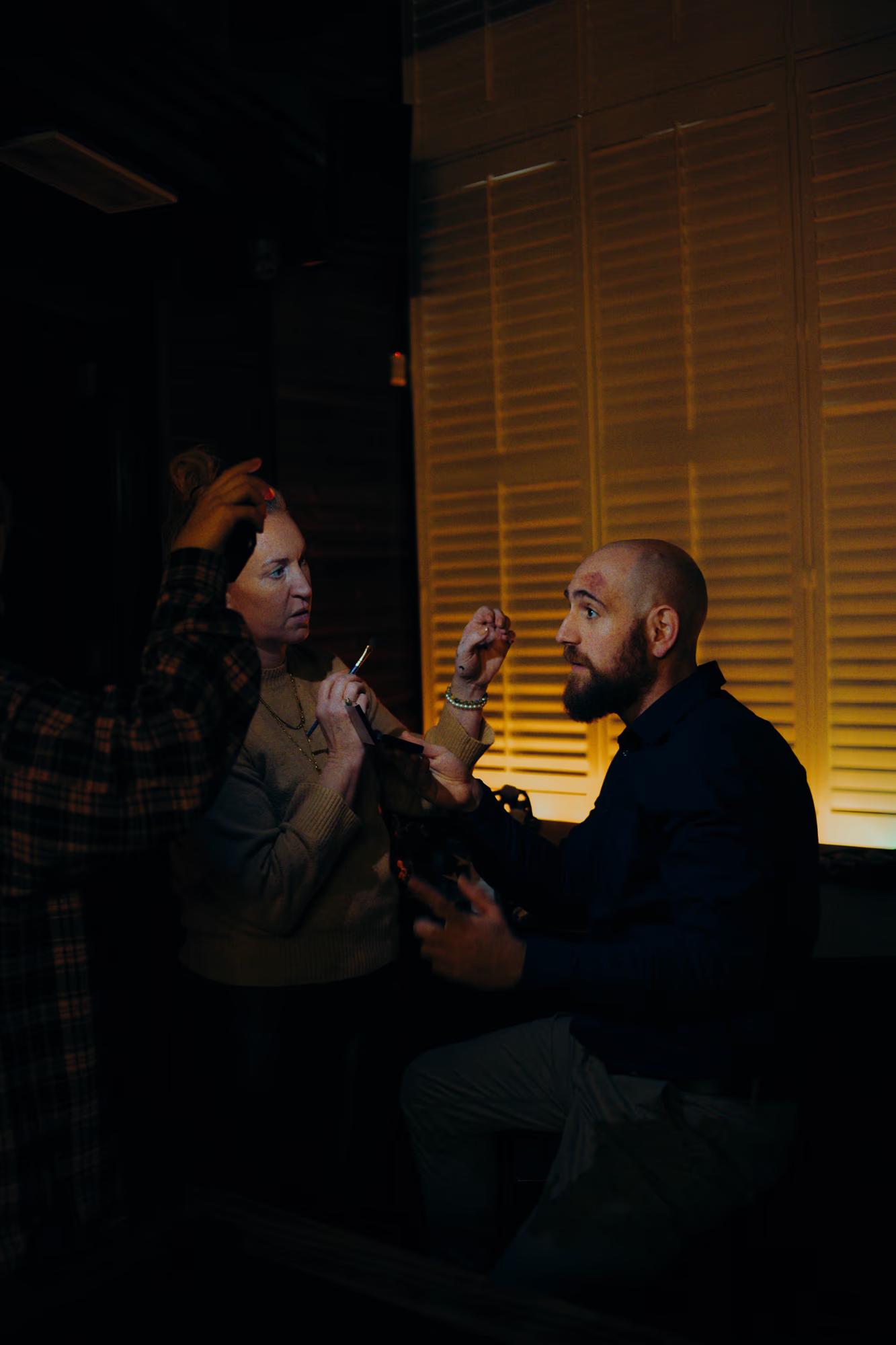 Close-up of actors in a confrontation scene, highlighted by warm, dramatic practical lighting on set.