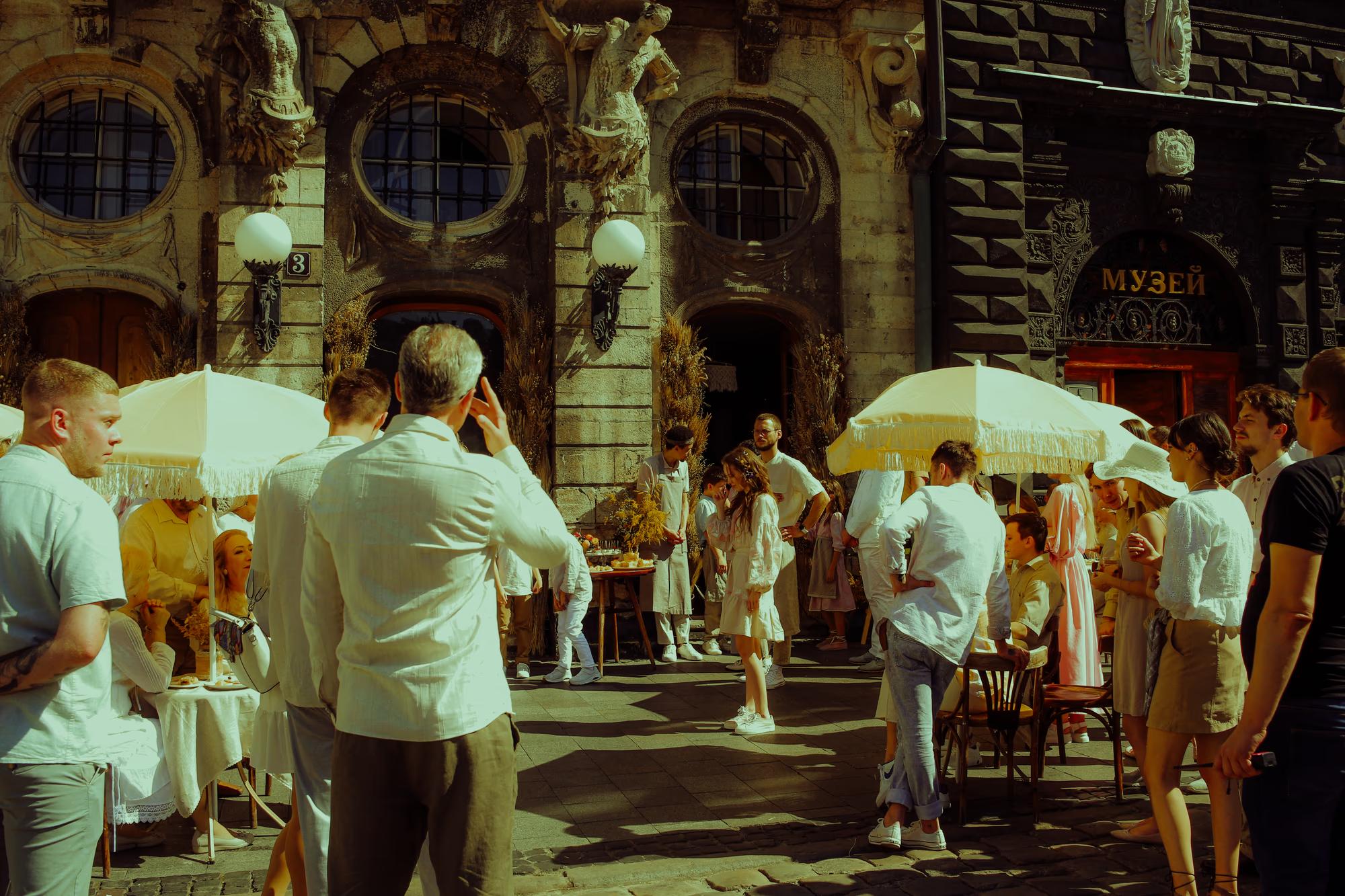 Action on set: Actors performing a scene in an outdoor cafe setting, captured from a behind-the-scenes perspective.