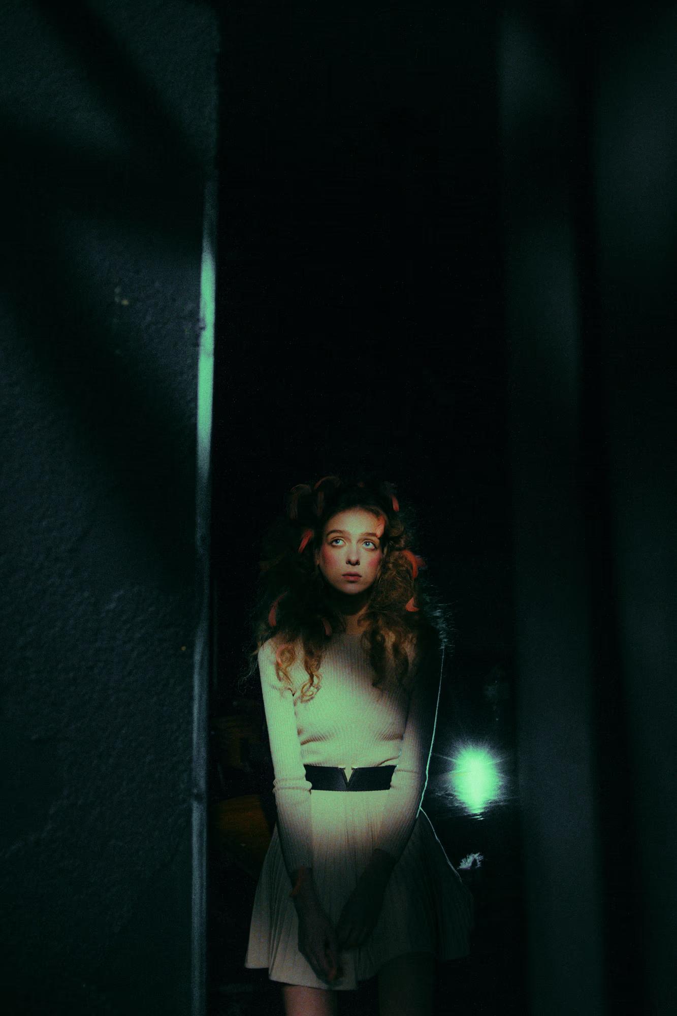High-fashion portrait framed by dark stage curtains, green ambient light.
