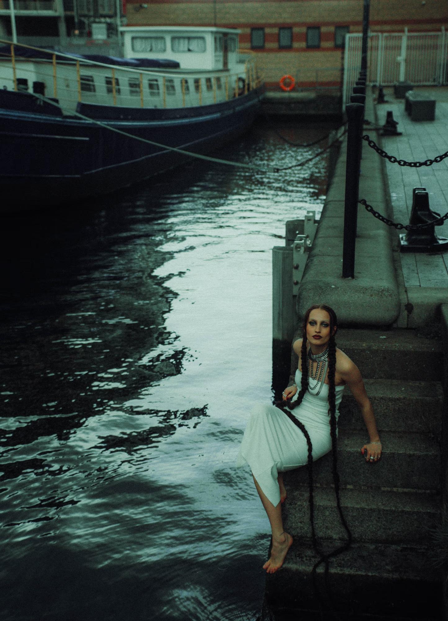 Dark moody medium shot of female model near waterfront with boat Canary Wharf London