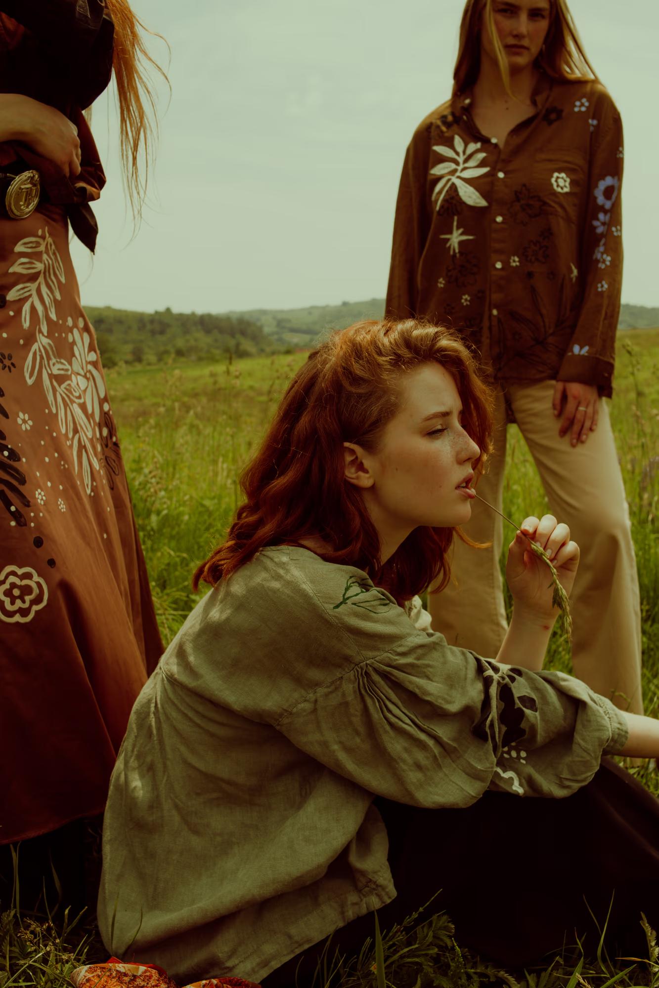 Medium fashion campaign shot of two women in Ukrainian designer ethnic outfits among red poppy field, warm film tones, Ukraine countryside editorial