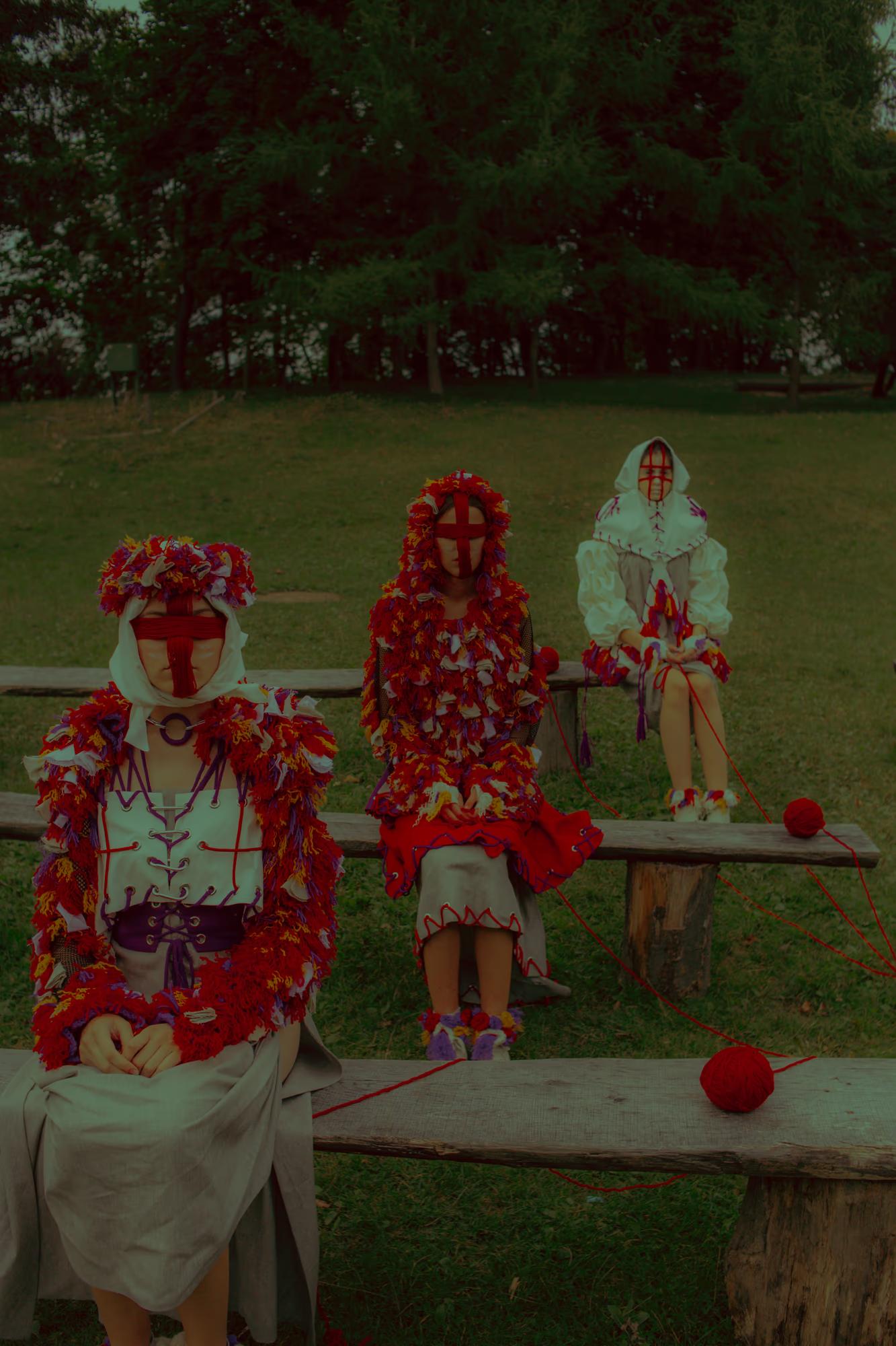 Editorial composition with models in red floral dresses sitting on a rustic bench, showcasing the harmony of nature and folk fashion.