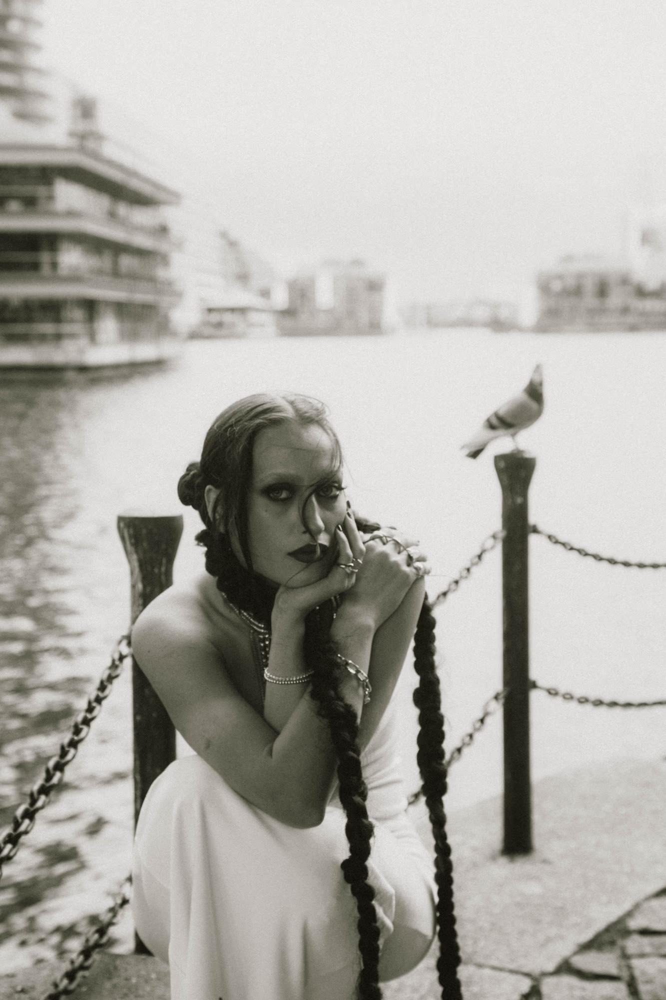 Medium shot of woman leaning on metal railing outdoors with a bird on a background, black and white film-style portrait, Canary Wharf London