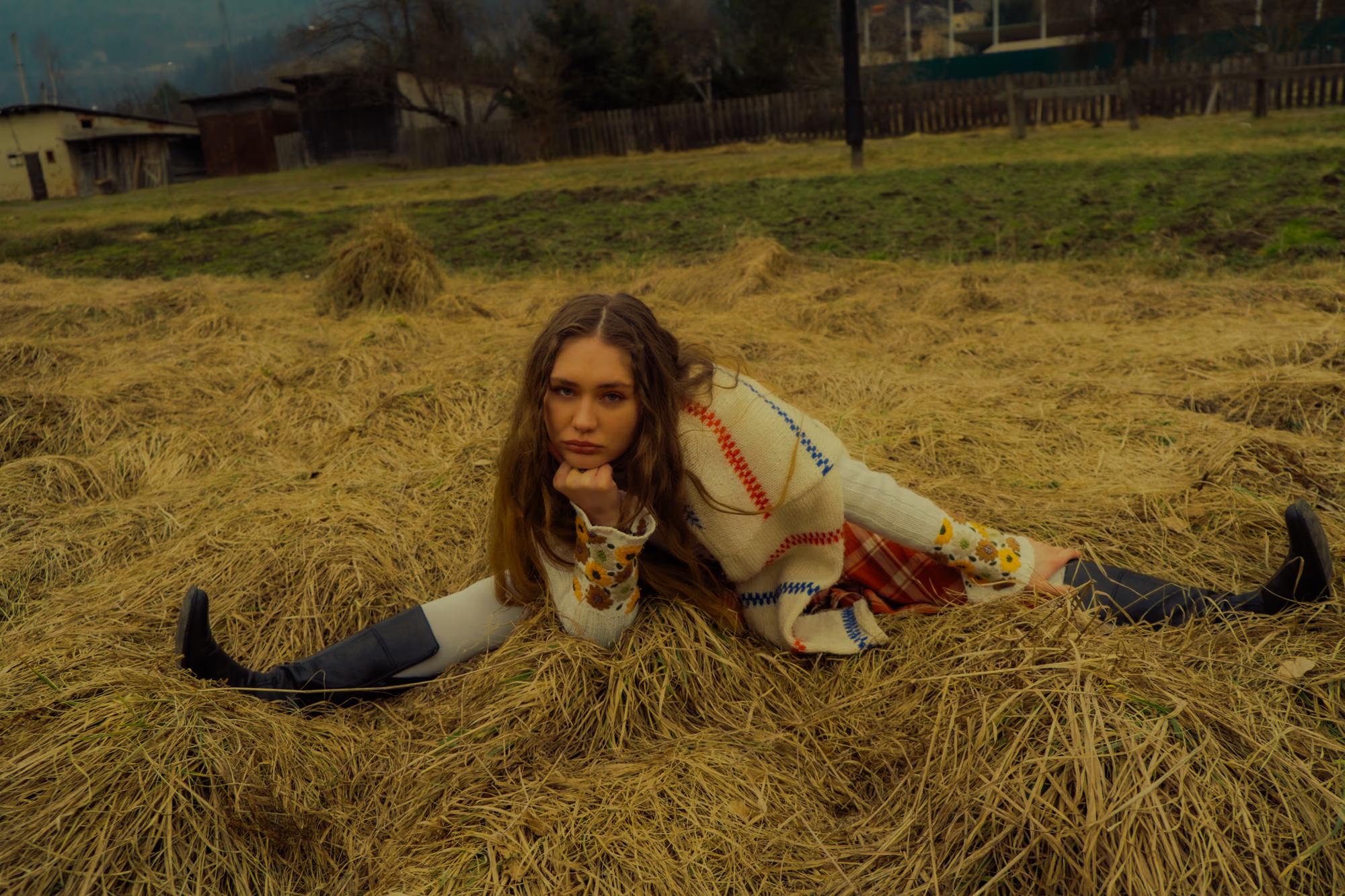 Full body fashion shot of woman in white blouse and tartan skirt sitting and lying in dry golden Carpathian meadow, relaxed natural pose, ethno editorial
