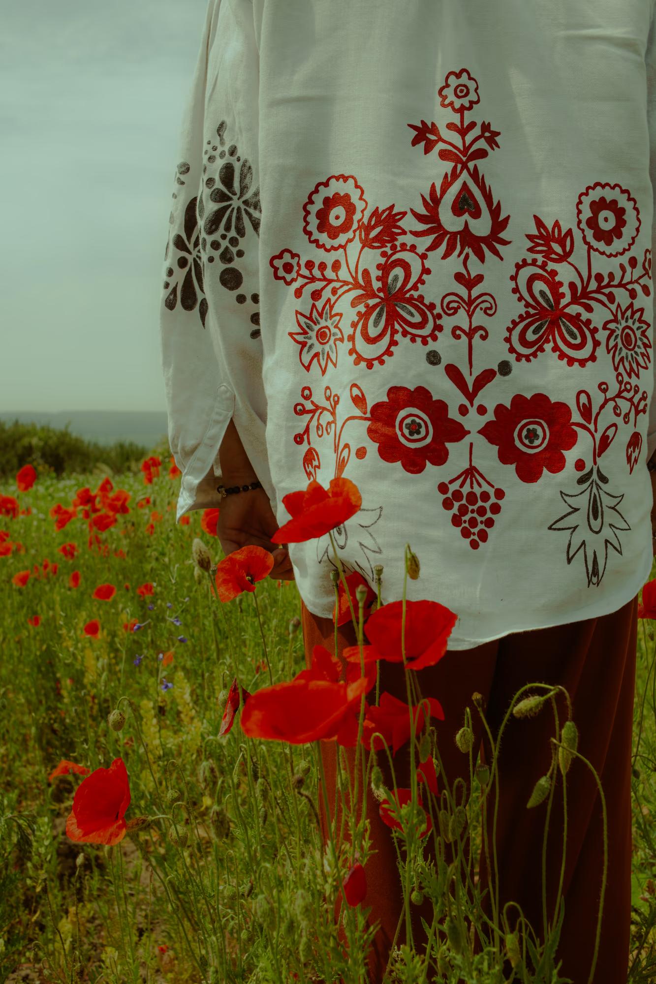 Close-up detail fashion shot of Ukrainian designer embroidered vyshyvanka blouse with red poppies in foreground, traditional Ukrainian fashion campaign