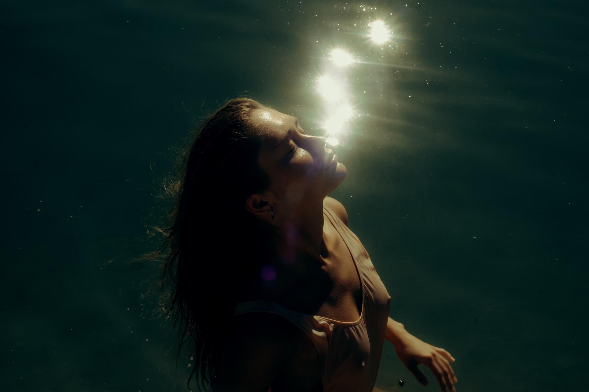 Underwater medium shot of woman submerged in dark teal lake water, soft diffused light from surface, cinematic fine art portrait