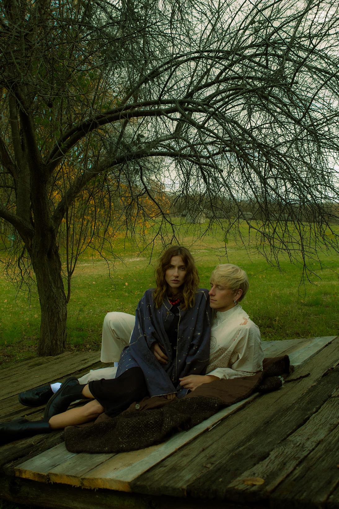Editorial fashion shot in Pirogovo open-air museum, models in minimalist ethnic wear by a vintage wooden house, Kyiv.