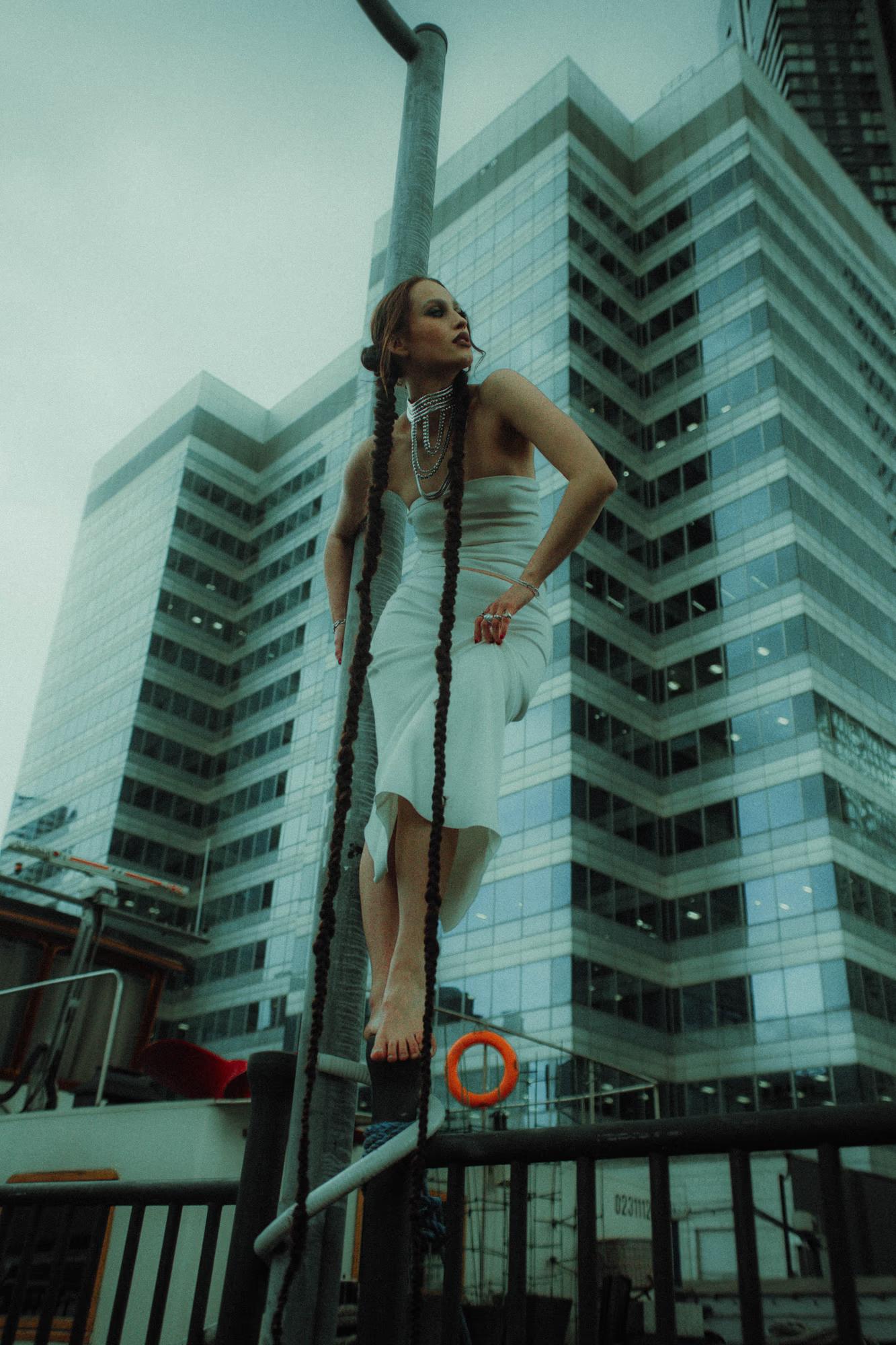 Full body shot of female model standing between two tall glass towers, teal architectural background, Canary Wharf London