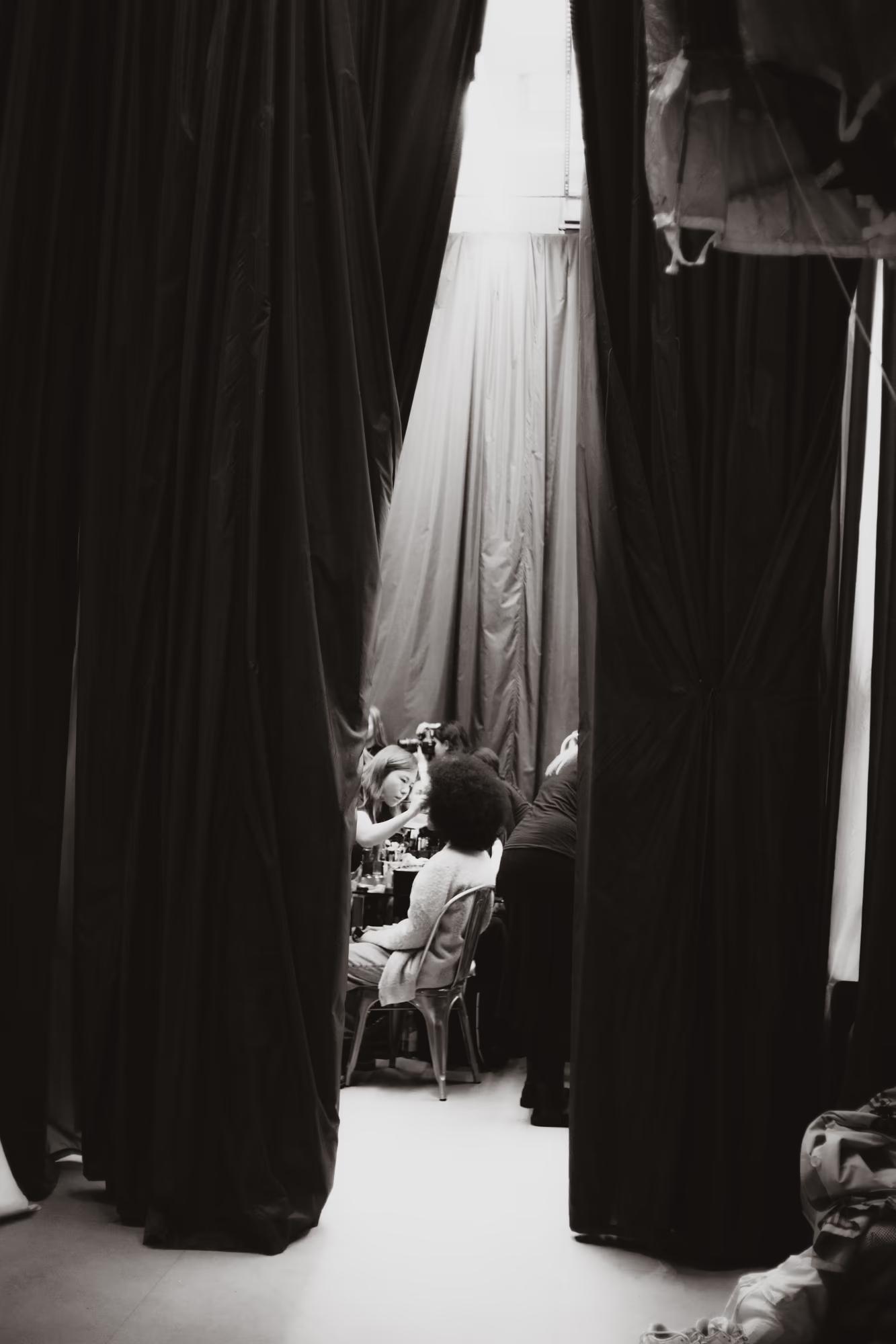 Peeking through heavy stage drapes: A glimpse into the intense preparation area of a professional fashion show.