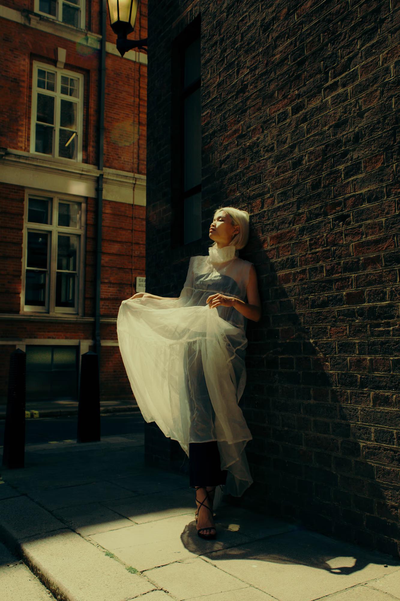 Model in elegant white dress near window, soft natural light fashion portrait, London streets