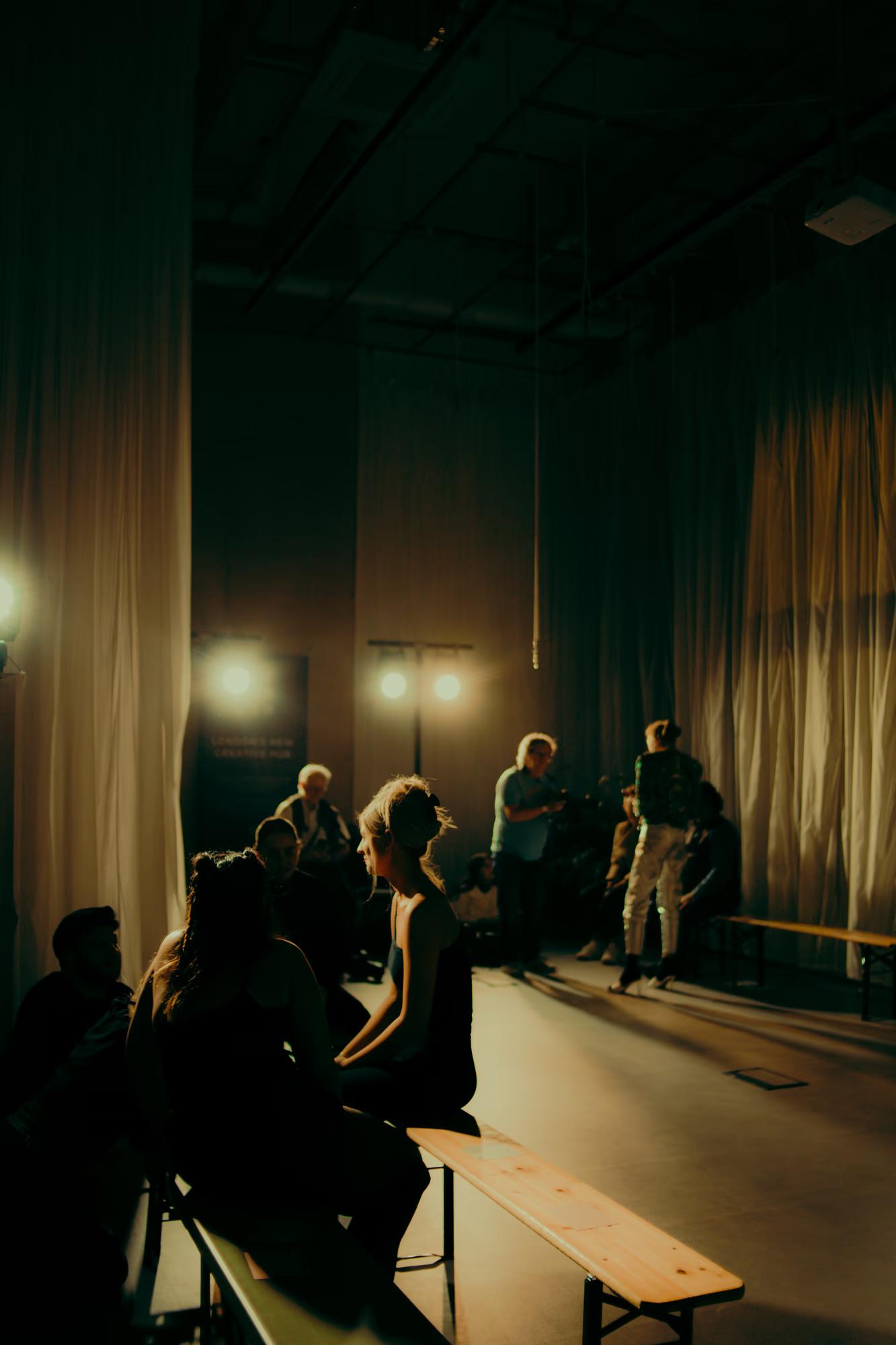Distant view of models and photographers in a dimly lit studio-style backstage setup at a fashion venue.