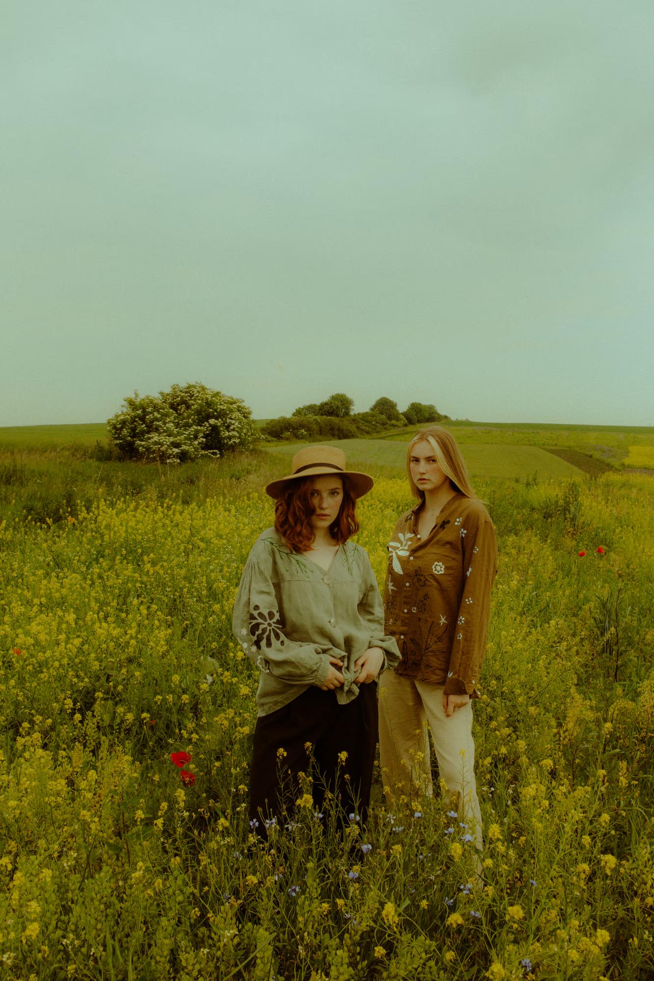 Full body wide fashion campaign shot of group of women in Ukrainian designer ethnic outfits in vast green poppy field, Ukraine countryside
