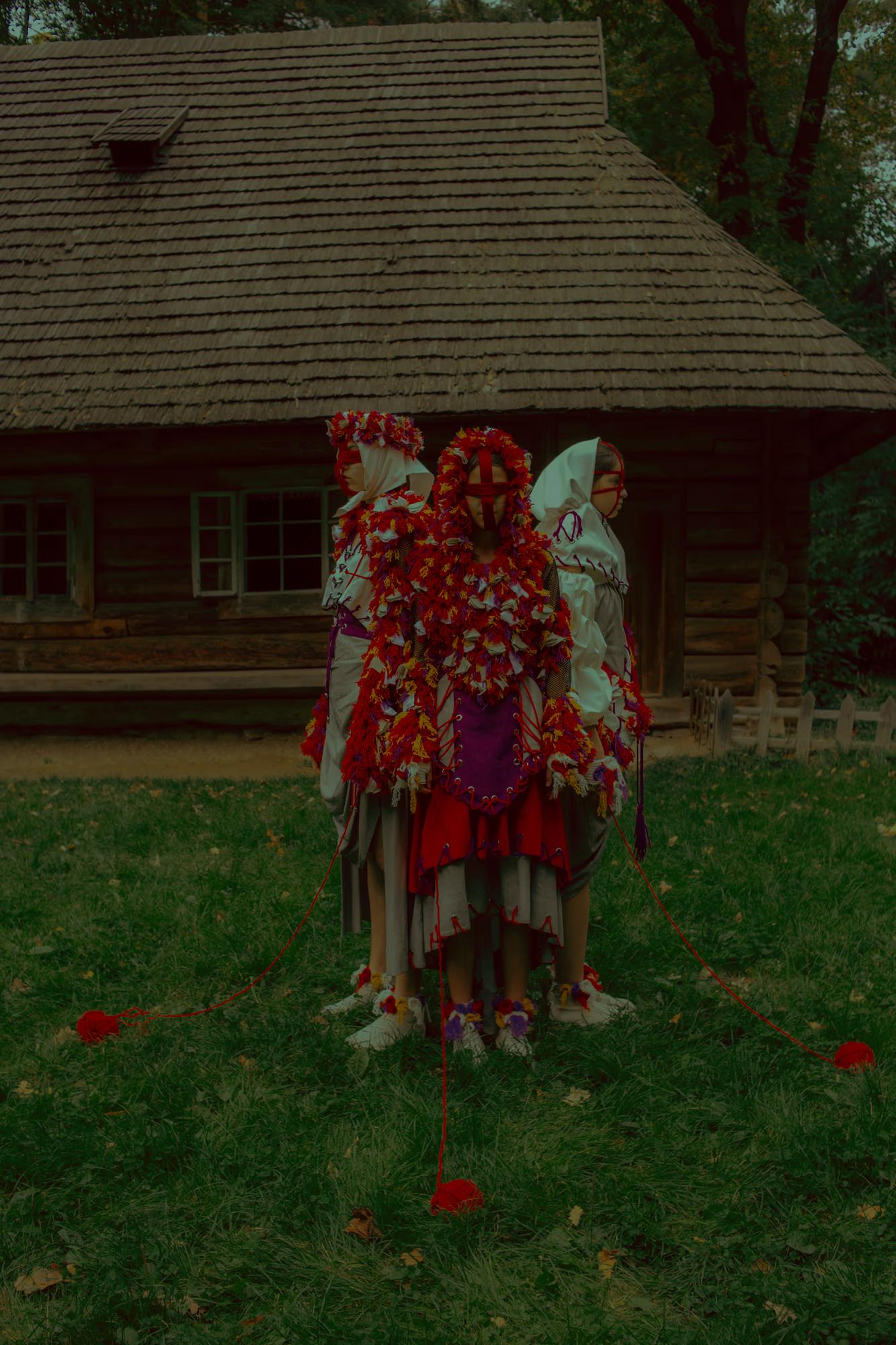 A model posing in the grass in front of a thatched-roof house, wearing a contemporary dress inspired by traditional Ukrainian embroidery.