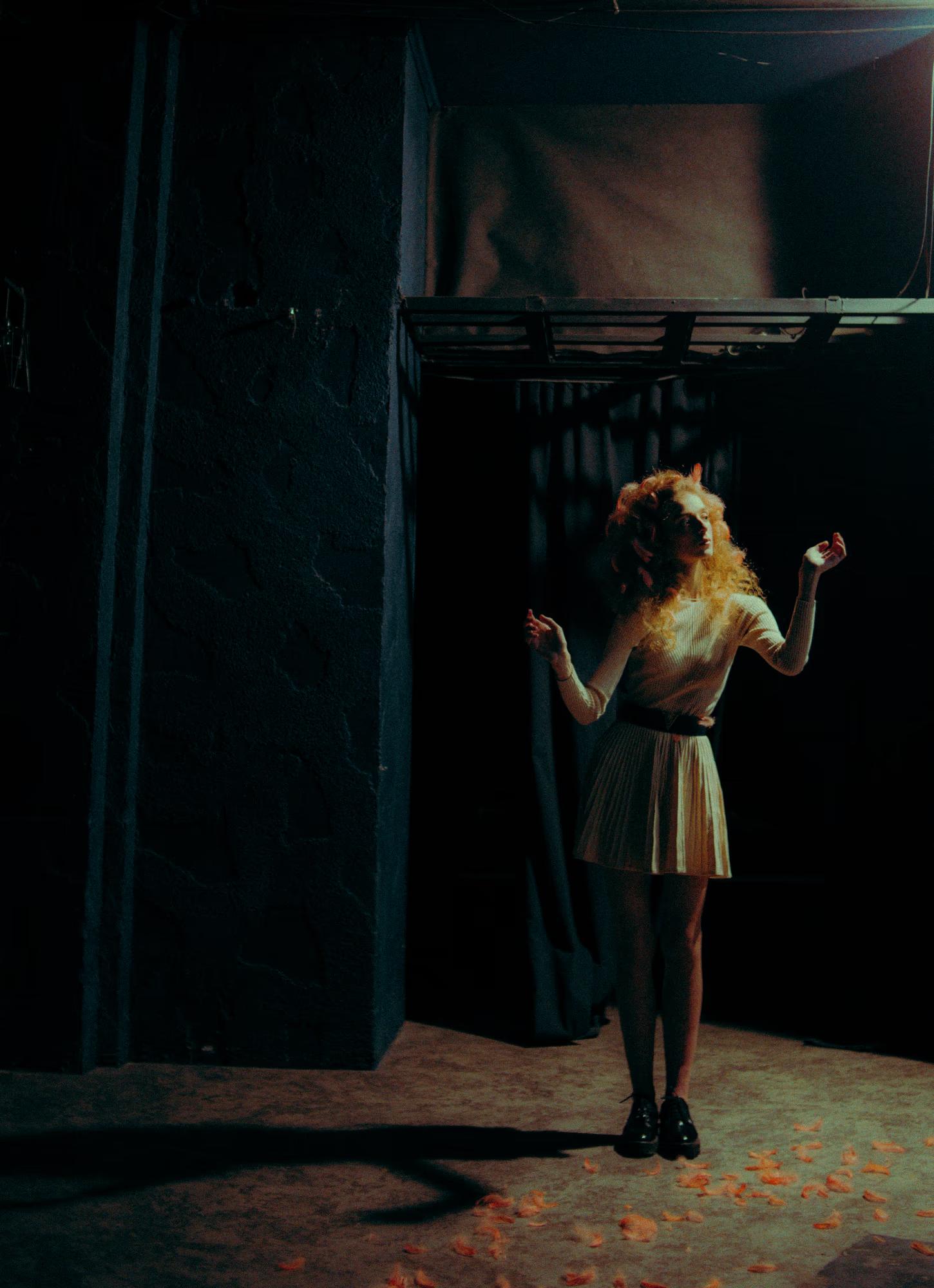 Behind-the-scenes style fashion shot of a woman in white on a dimly lit stage.