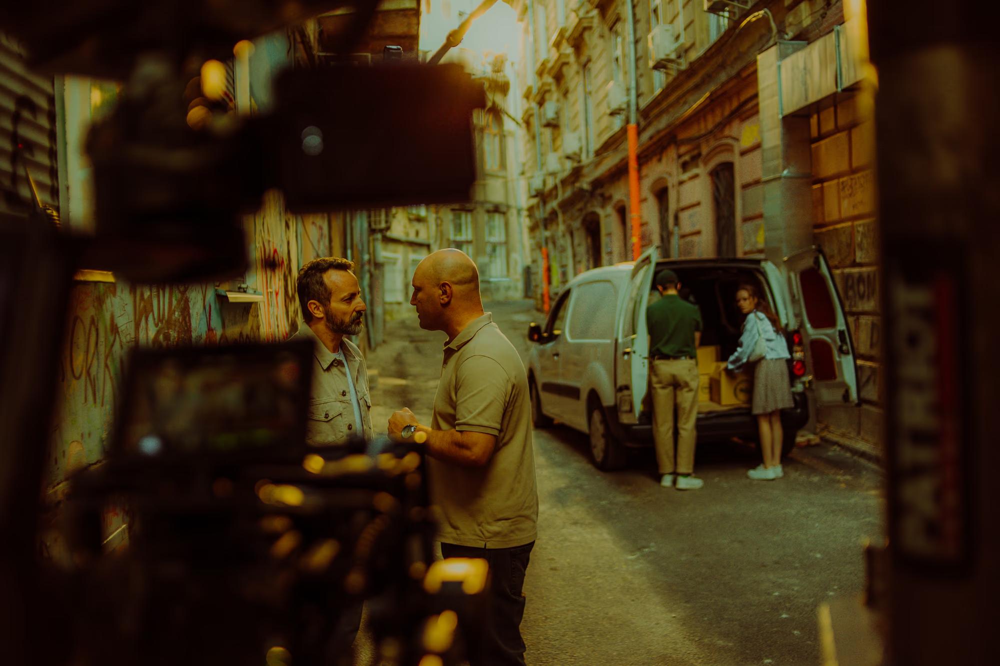 Wide shot of a busy film set interior, showing production equipment, lighting rigs, and the creative crew at work.