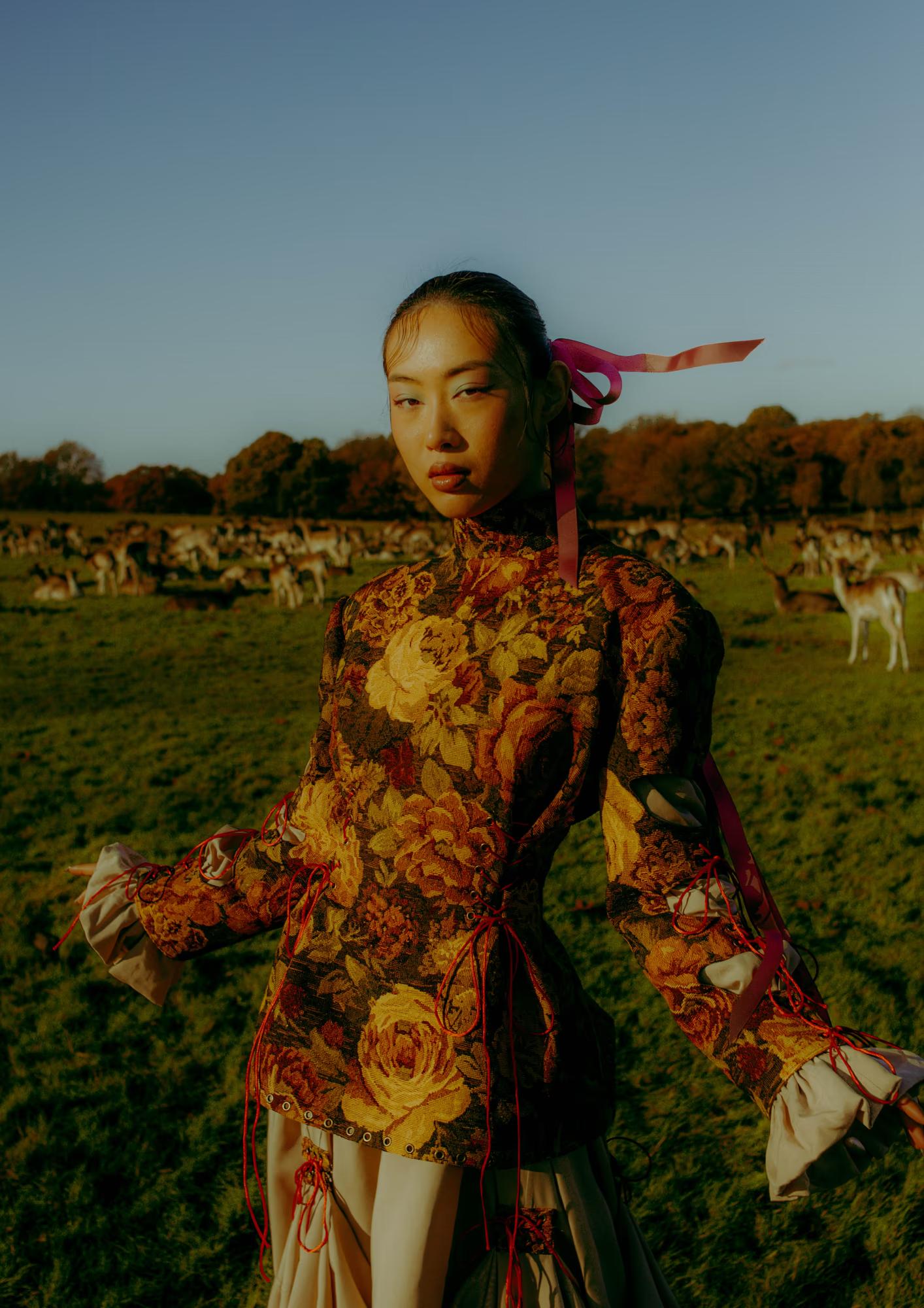 Full body fashion campaign shot of woman in vibrant floral designer outfit with arms outstretched in open field, Richmond Park London, golden hour editorial