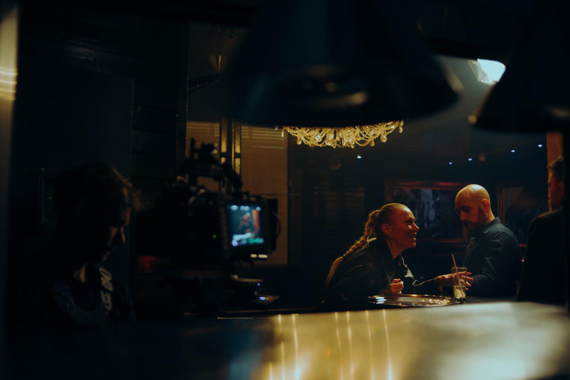 Behind-the-scenes: Camera crew filming a tense dialogue scene in a dimly lit London pub setting.