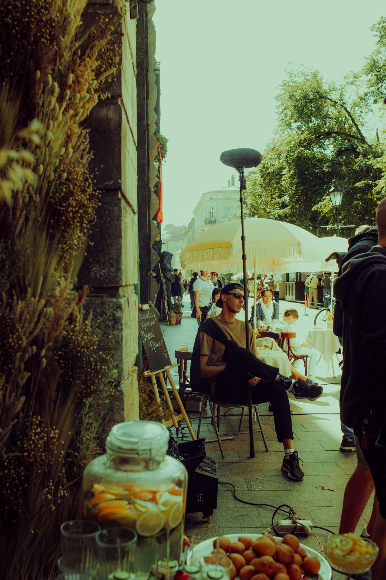 Atmospheric shot of a production assistant near large lighting diffusers on a sunny outdoor film set.