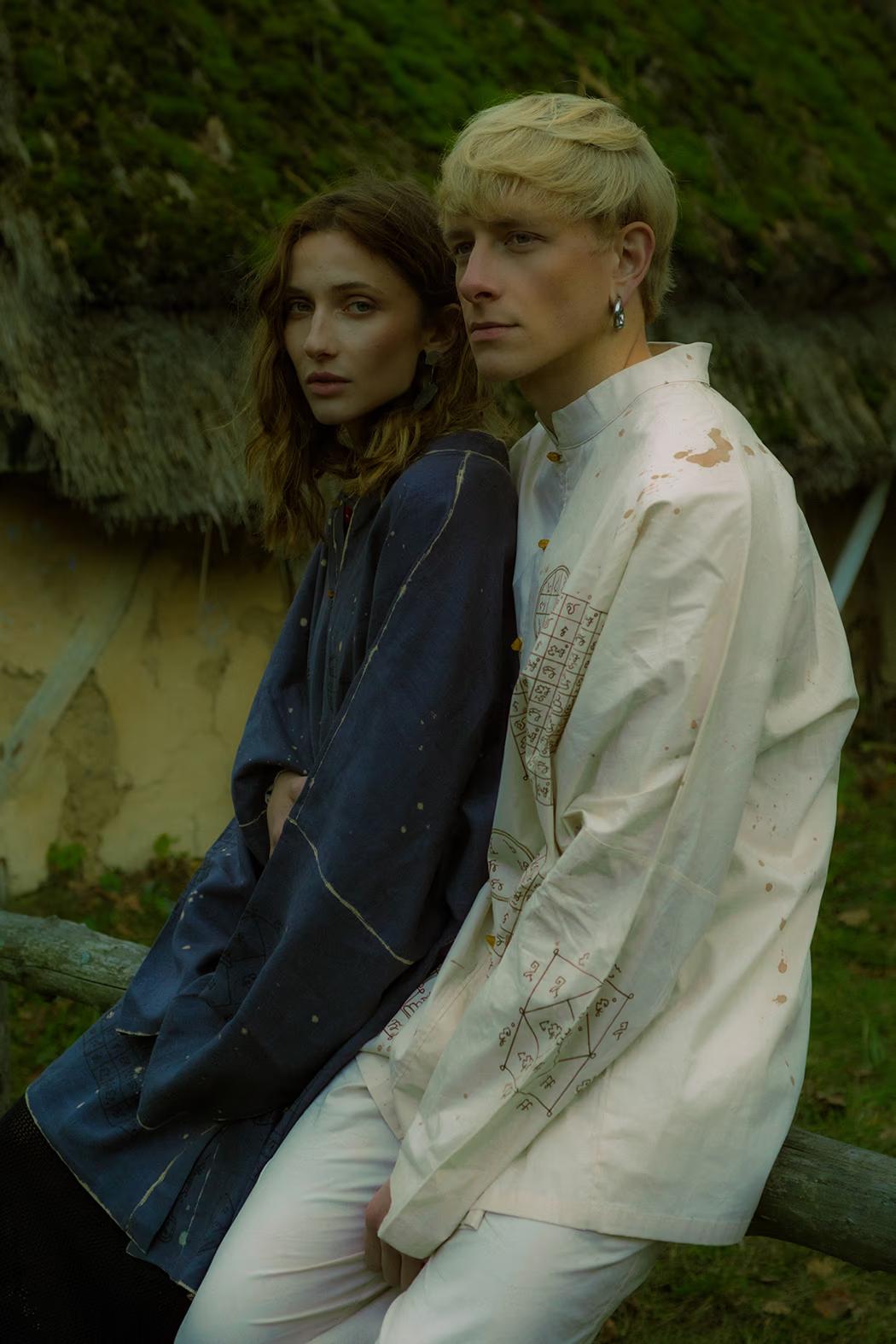 Models in avant-garde ethno-wear posing by weathered stone and wood structures, Pirogovo open-air museum setting.