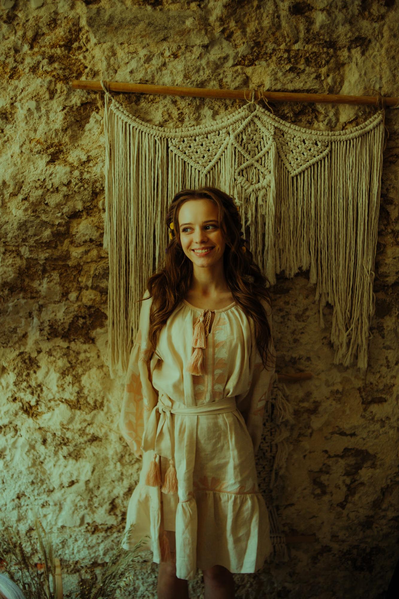 Artistic shot of a model standing against a textured historic wall, soft natural lighting and film grain.