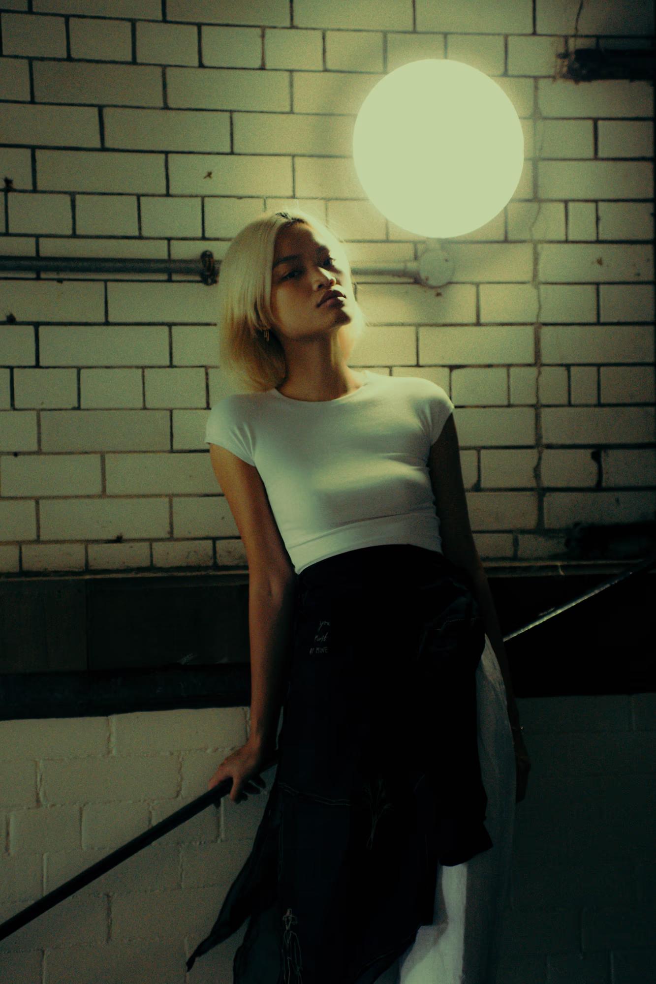 Blonde Filipino model posing against tiled wall with lamp, editorial fashion shoot with vintage tones