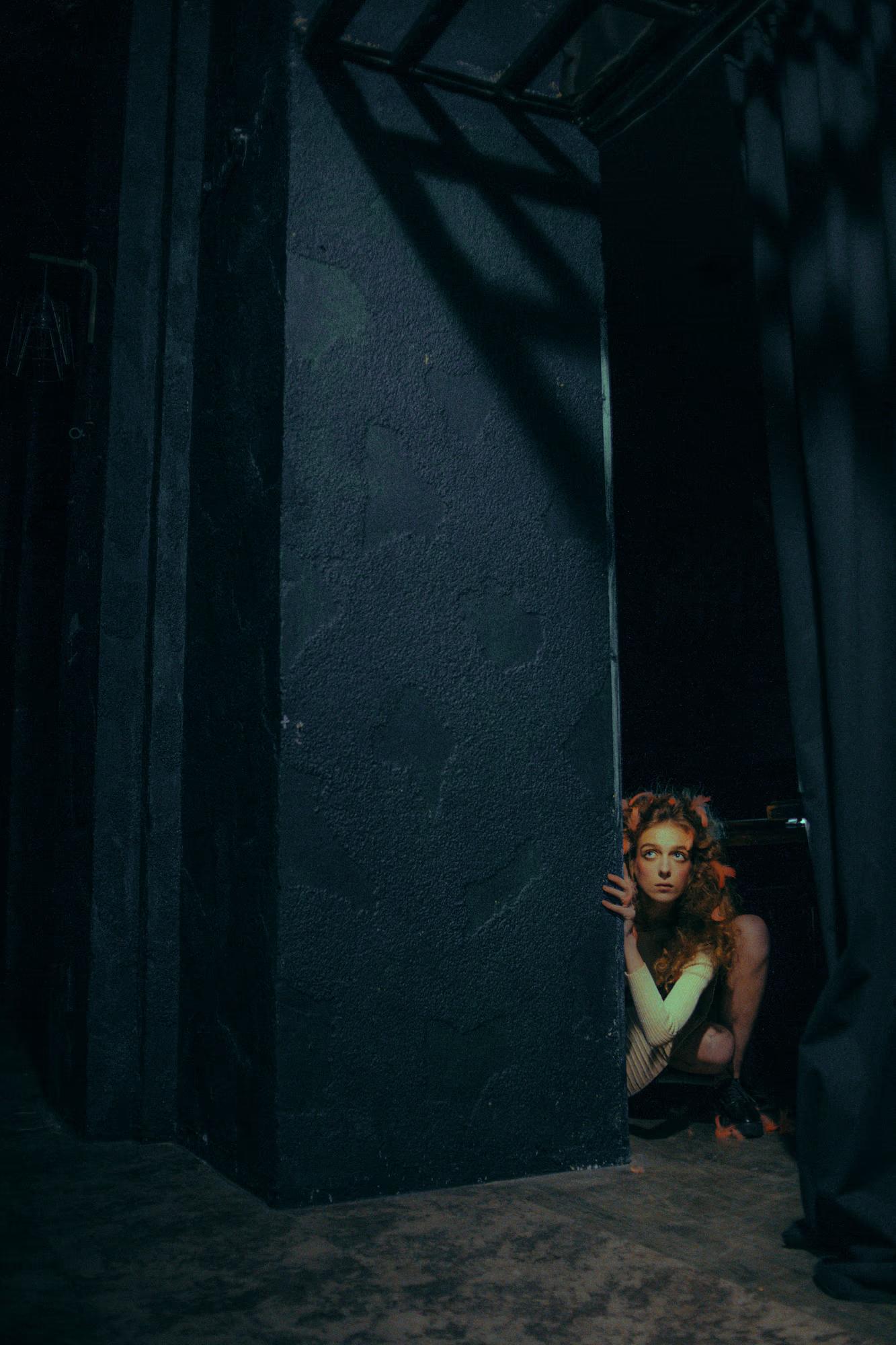 Conceptual fashion photo of a model blending into deep shadows of a theater set.