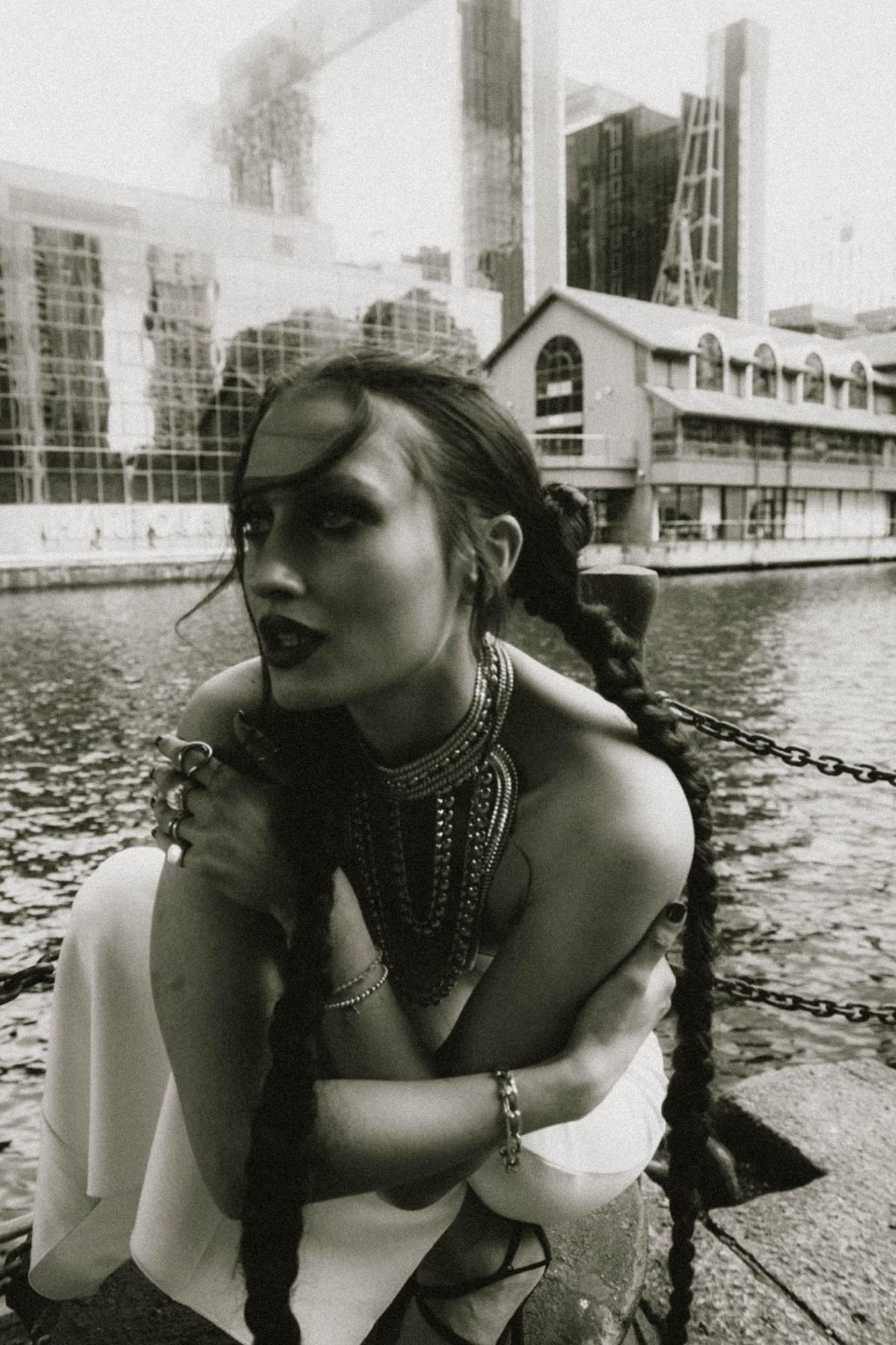 Close-up black and white portrait of woman leaning against railing with urban architecture background, Canary Wharf London