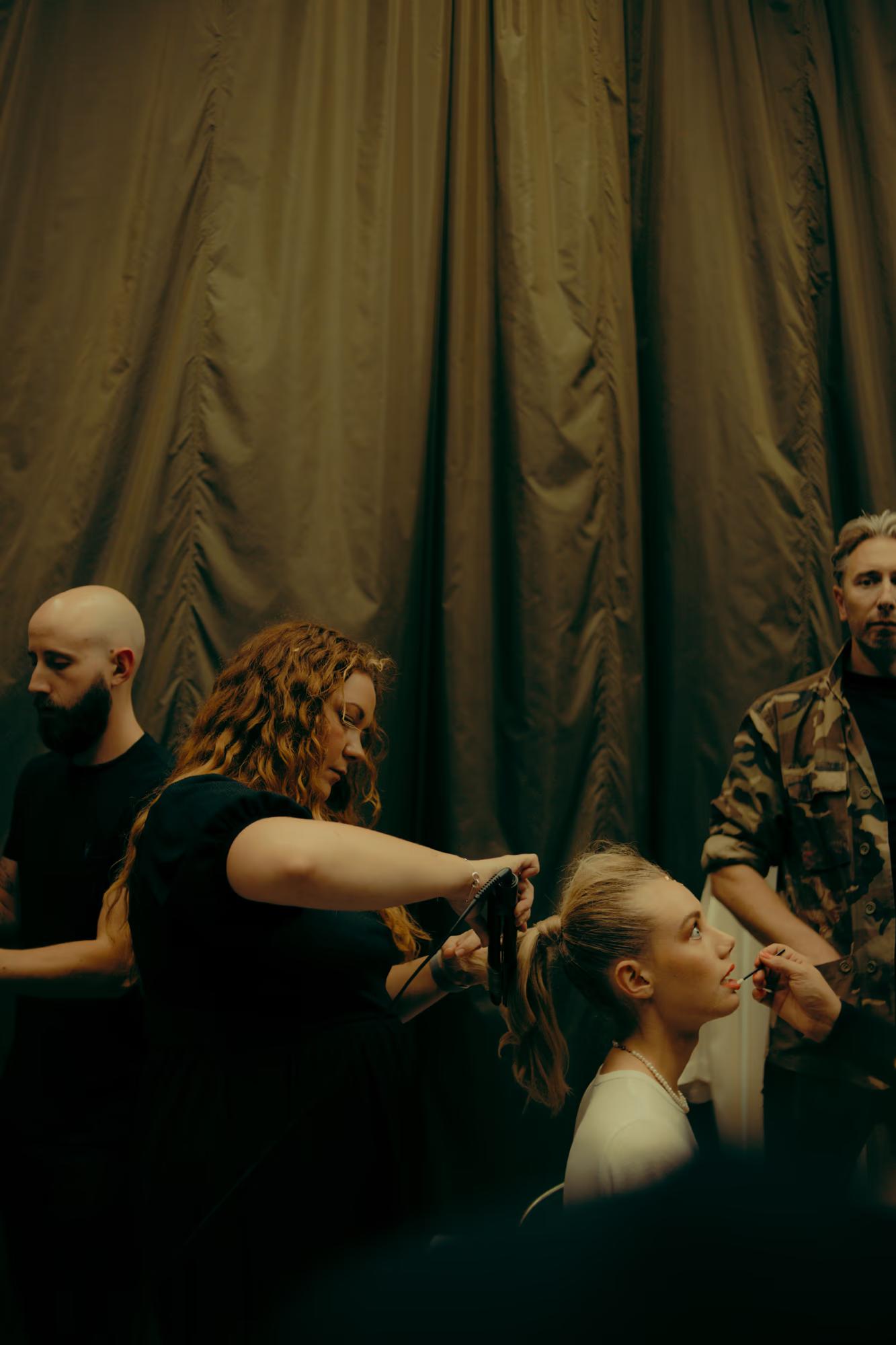 Busy dressing area: Makeup artists and models in a low-lit, golden-hued backstage setting at LFW.