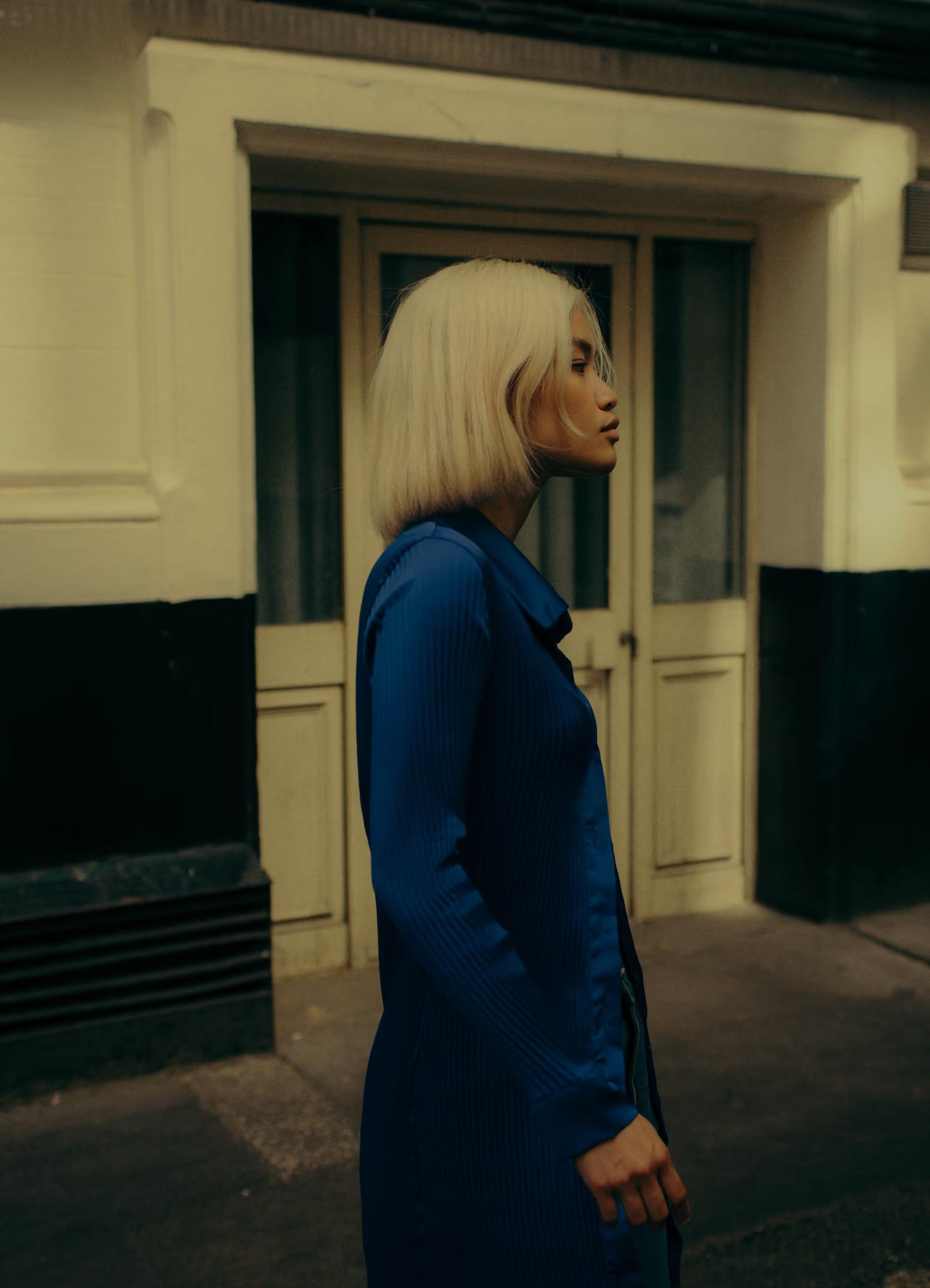 Blonde  Filipino model in blue dress standing in urban doorway, cinematic fashion portrait