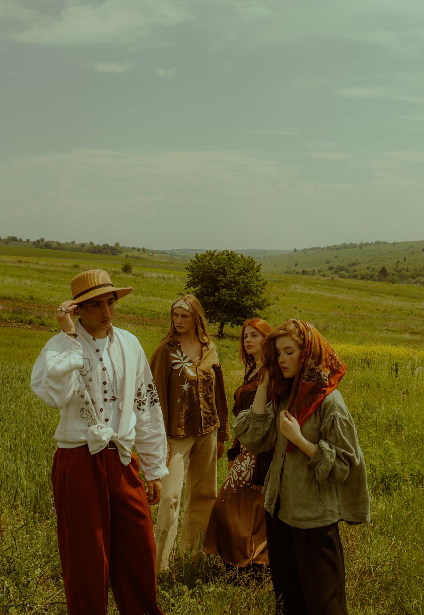 Full body fashion campaign shot of two women in Ukrainian designer ethnic outfits standing in vast green poppy field, overcast sky, Ukraine editorial