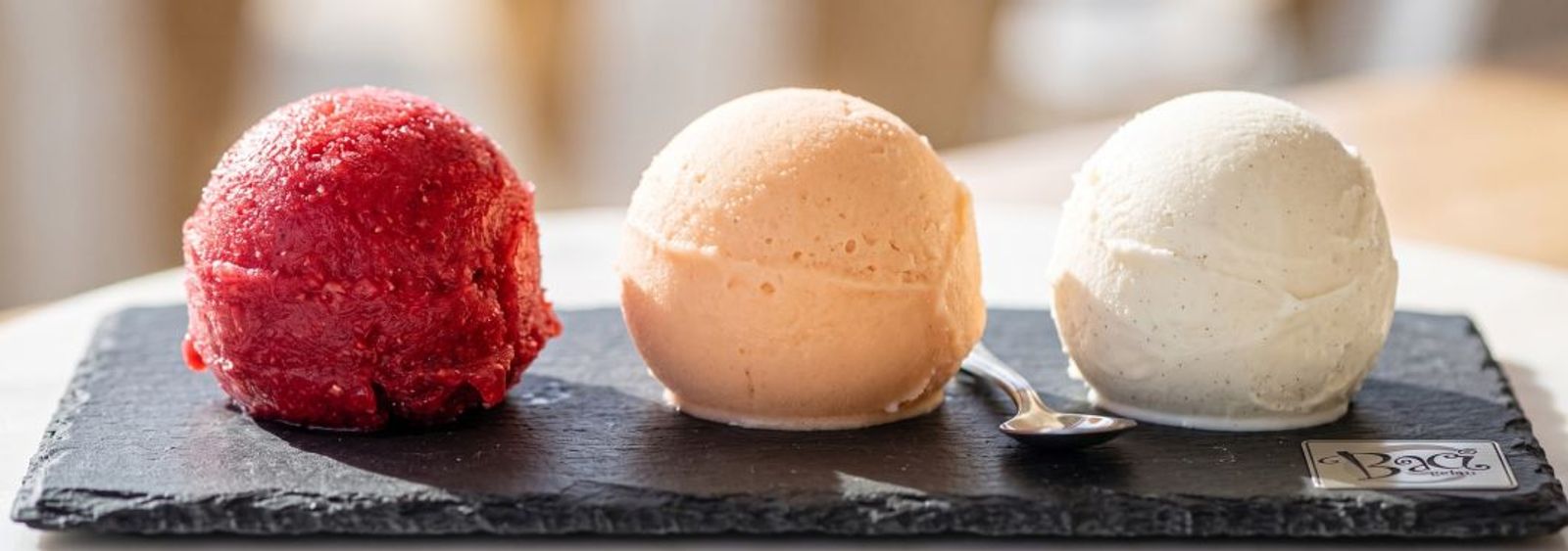 Scoops of bright fruit sorbet and pale sherbet in chilled steel pans