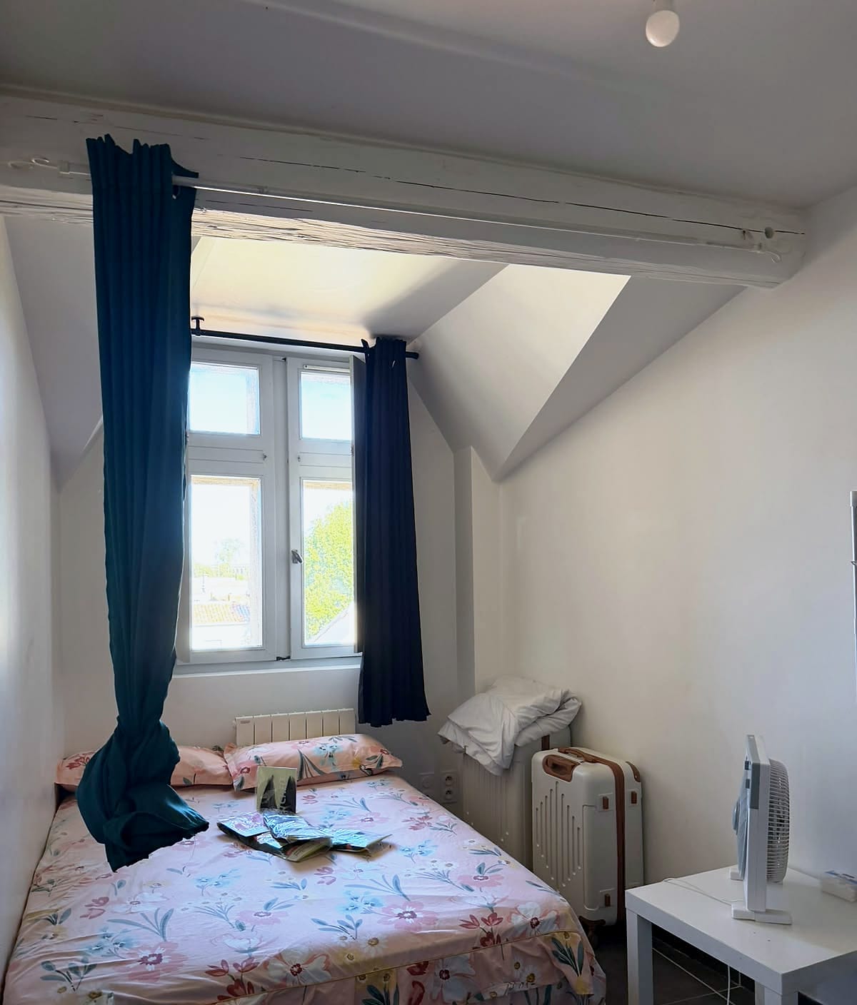 Chambre avec poutre apparente et fenêtre donnant sur les toits