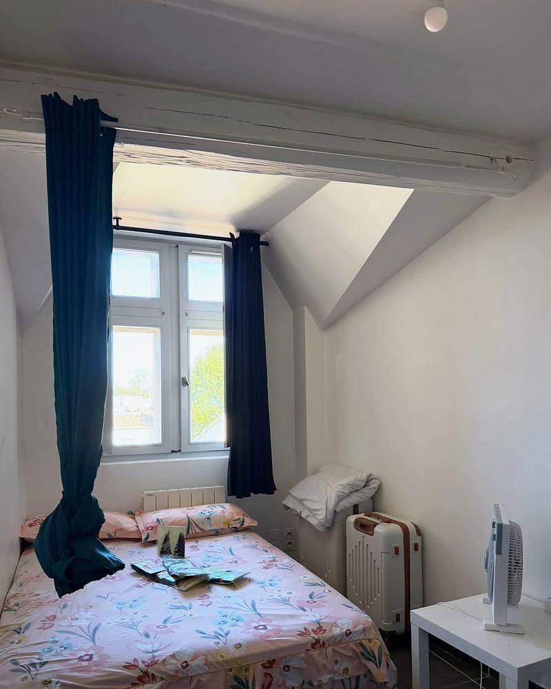 Chambre avec poutre apparente et fenêtre donnant sur les toits