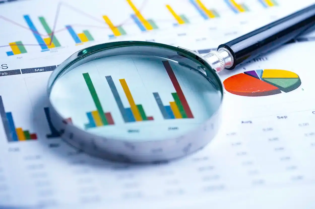 Una lupa sobre las gráficas de barras y de sectores impresas de un informe financiero.