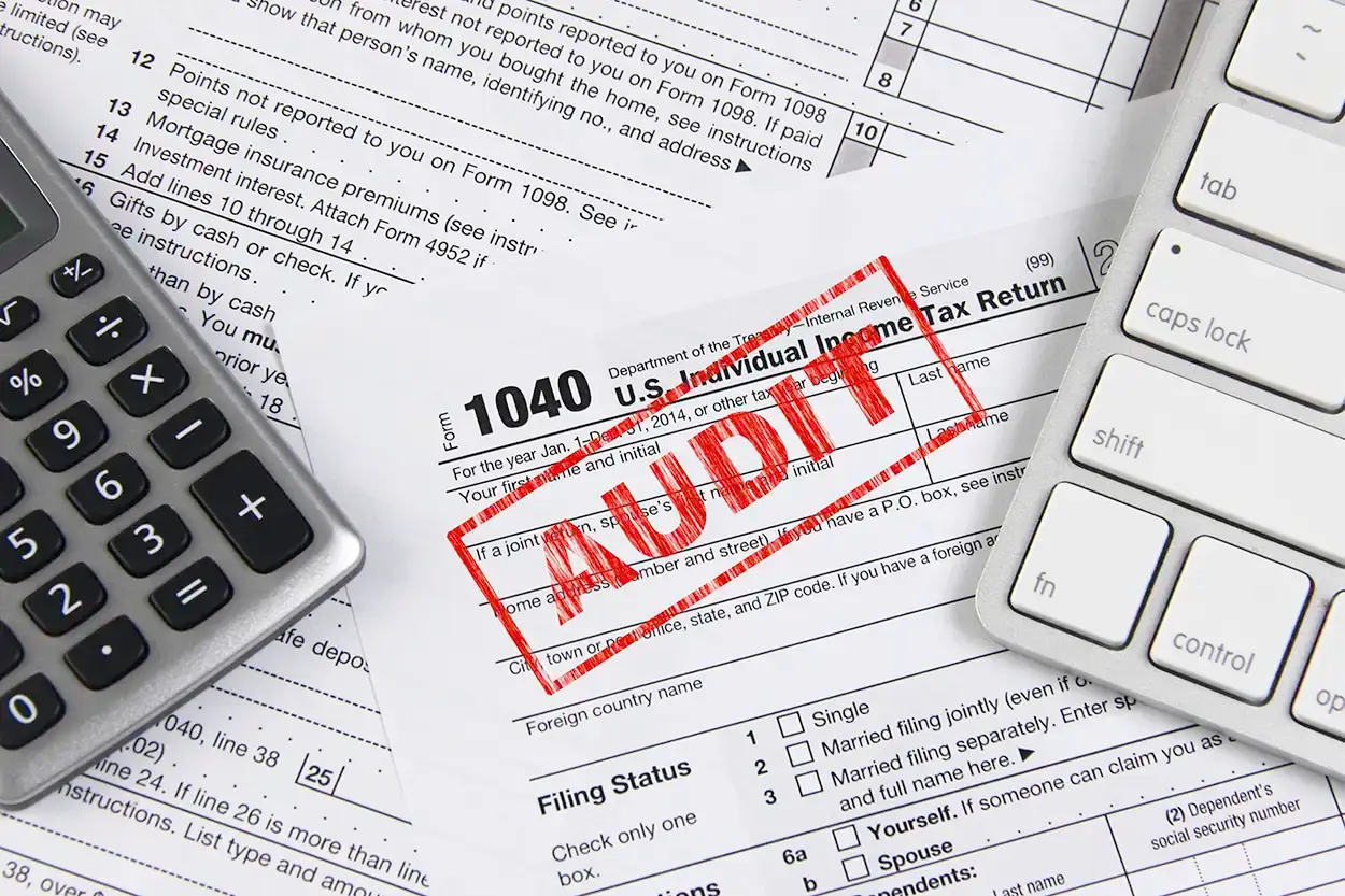 Una declaración Form 1040 con un sello rojo que dice AUDIT, junto a una calculadora y un teclado.