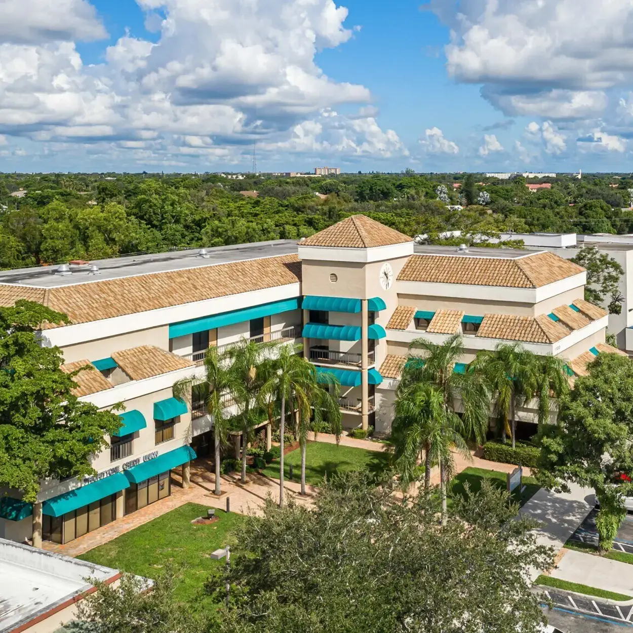 Vista aérea del edificio de oficinas de tres plantas, con tejado de teja y toldos color verde azulado, en 1700 N University Drive, Coral Springs, Florida