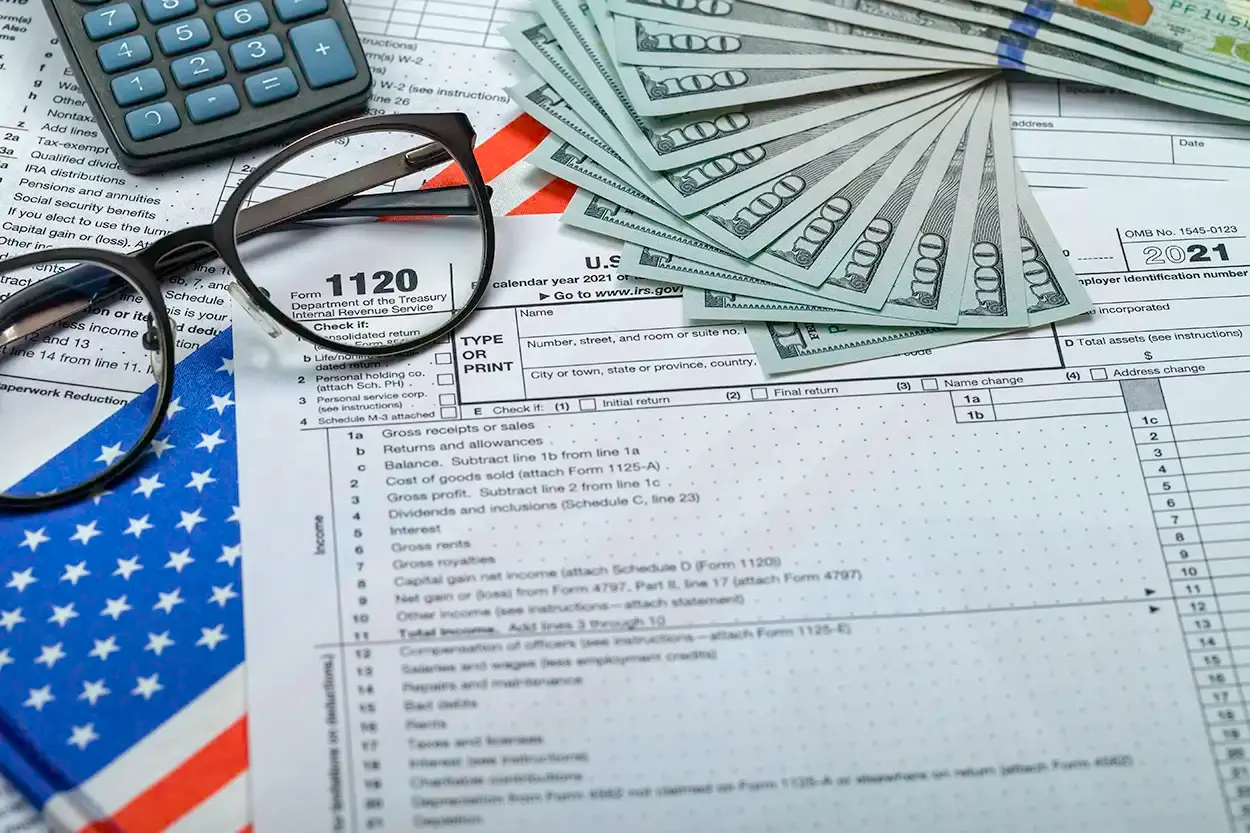 Formularios de declaración de impuestos impresos, con unas gafas, una calculadora, billetes y una bandera de Estados Unidos.