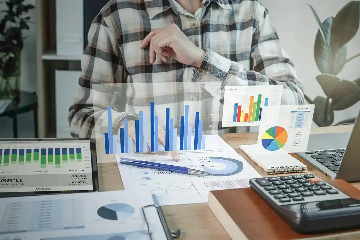 Una persona revisando en su escritorio informes impresos con gráficas de barras y de sectores, junto a una calculadora.