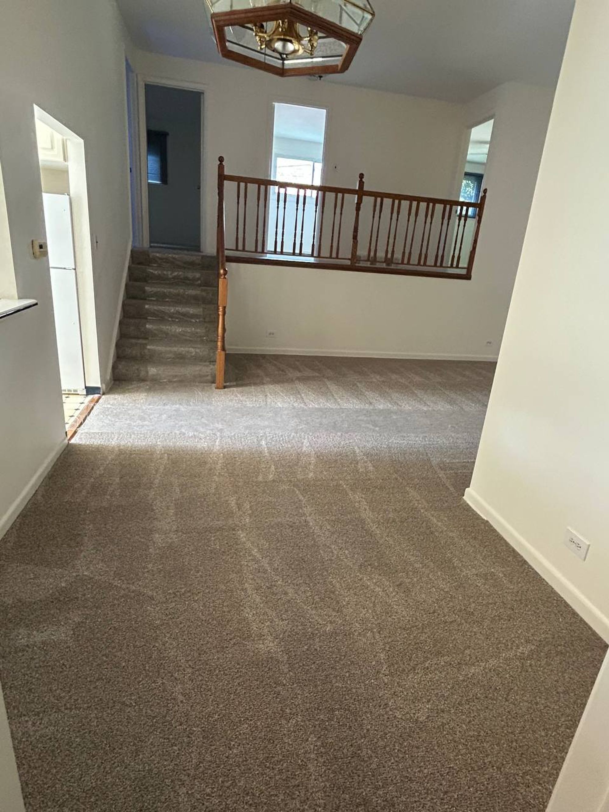 Empty split level room with carpeted stairs and wood railing