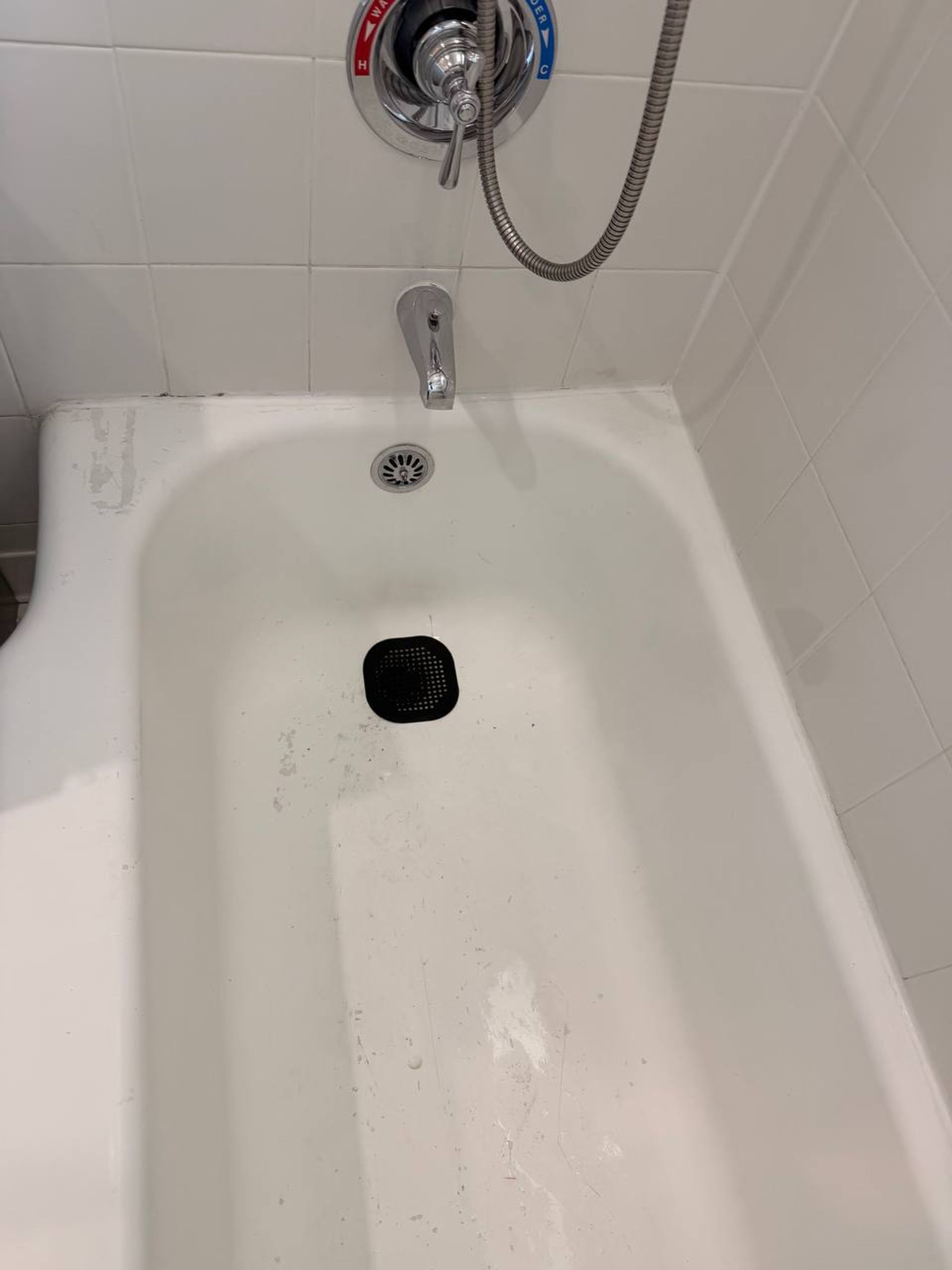 Scrubbed white bathtub with chrome handle and handheld shower hose