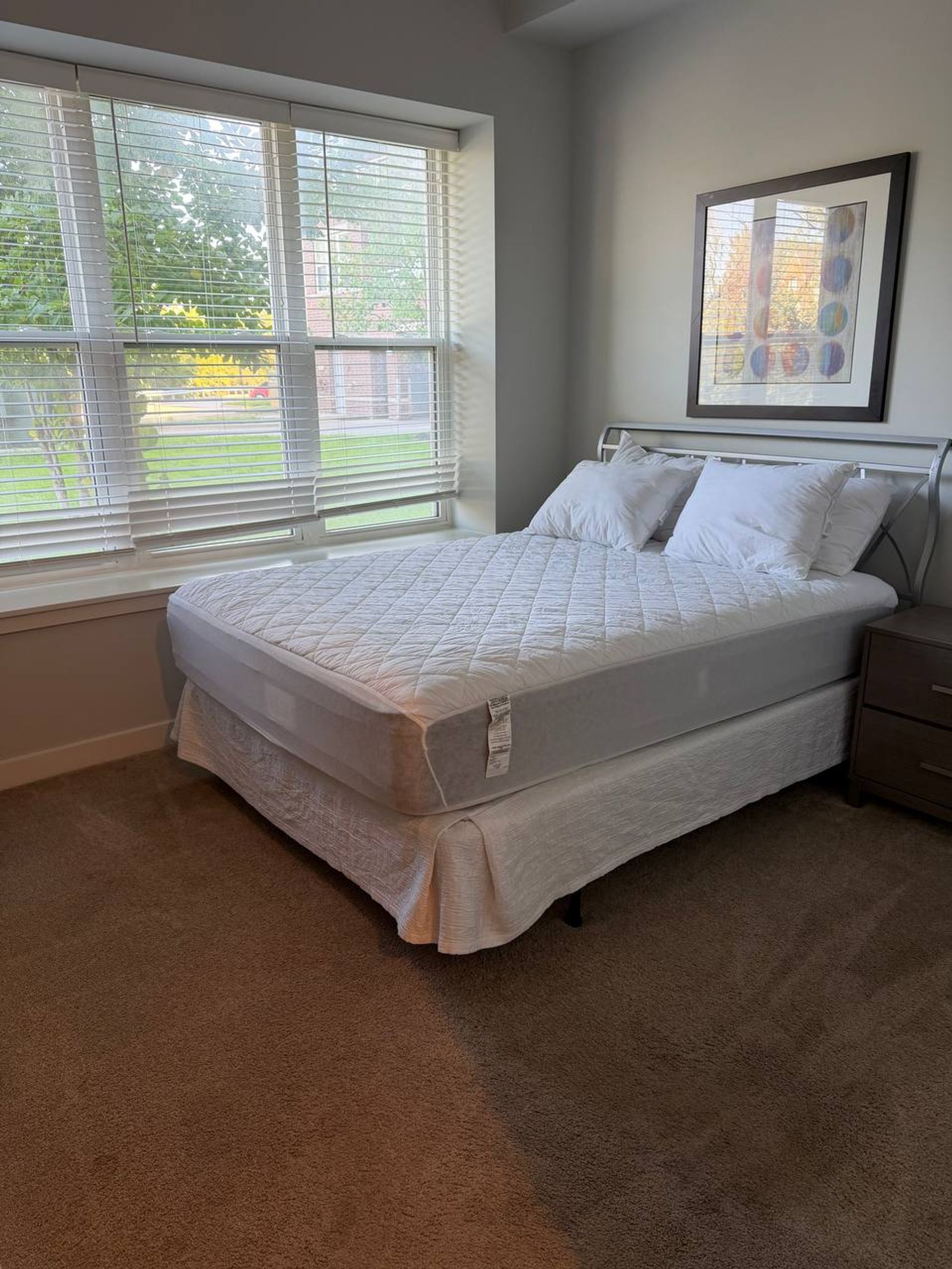 Bedroom with bare mattress, white pillows and framed art