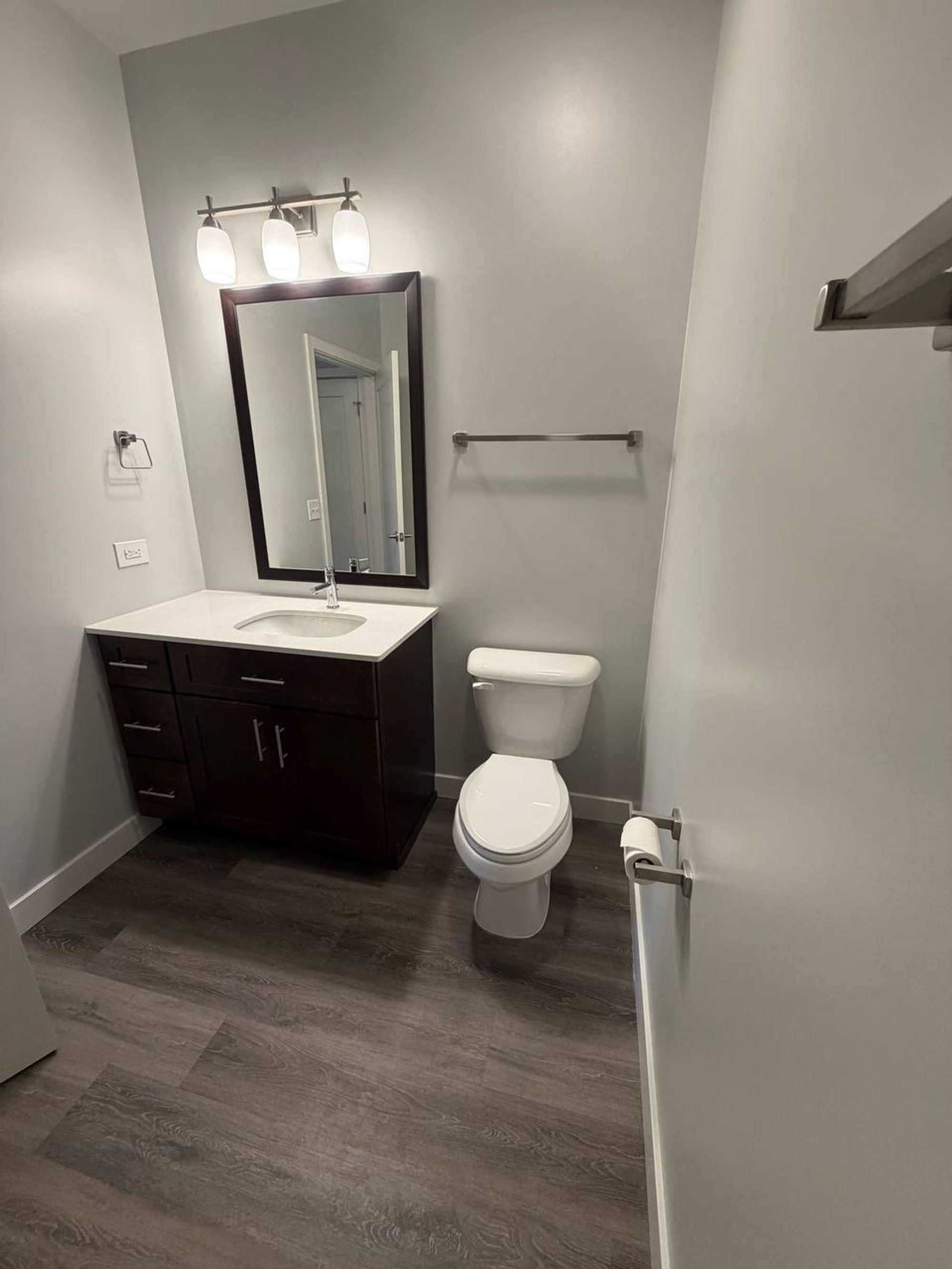 Half bath with dark vanity, framed mirror and wood-look floor