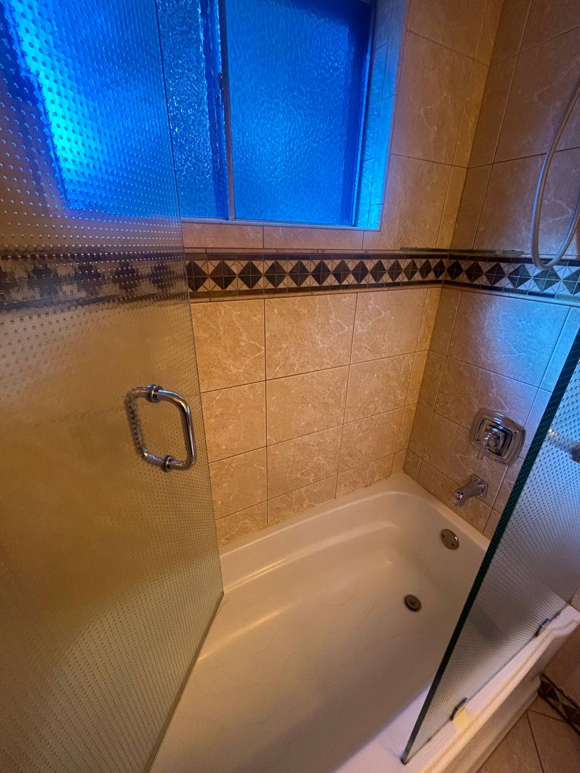 White tub behind dotted glass doors with beige tile and diamond border