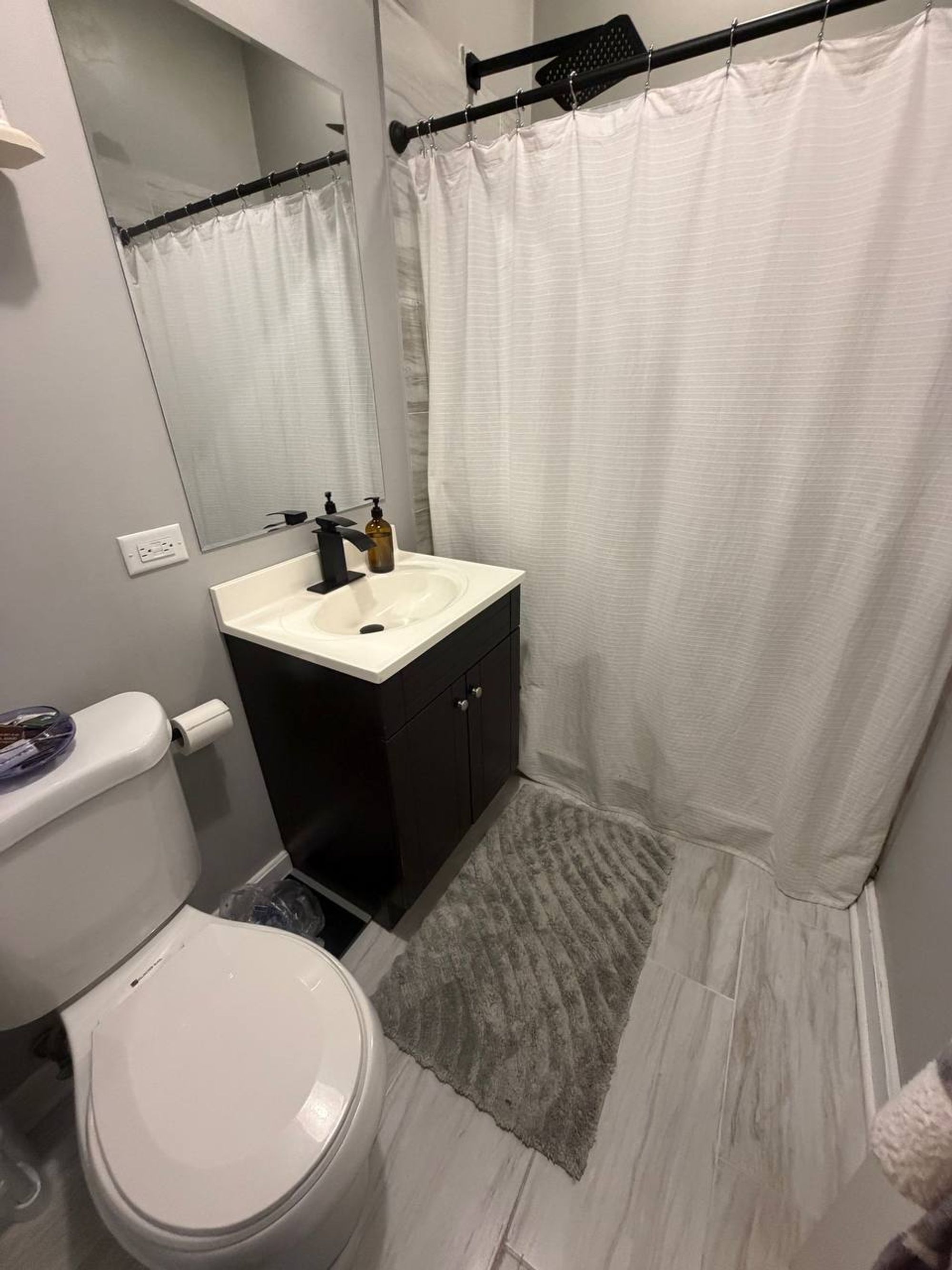 Small bathroom with white shower curtain, dark vanity and gray mat