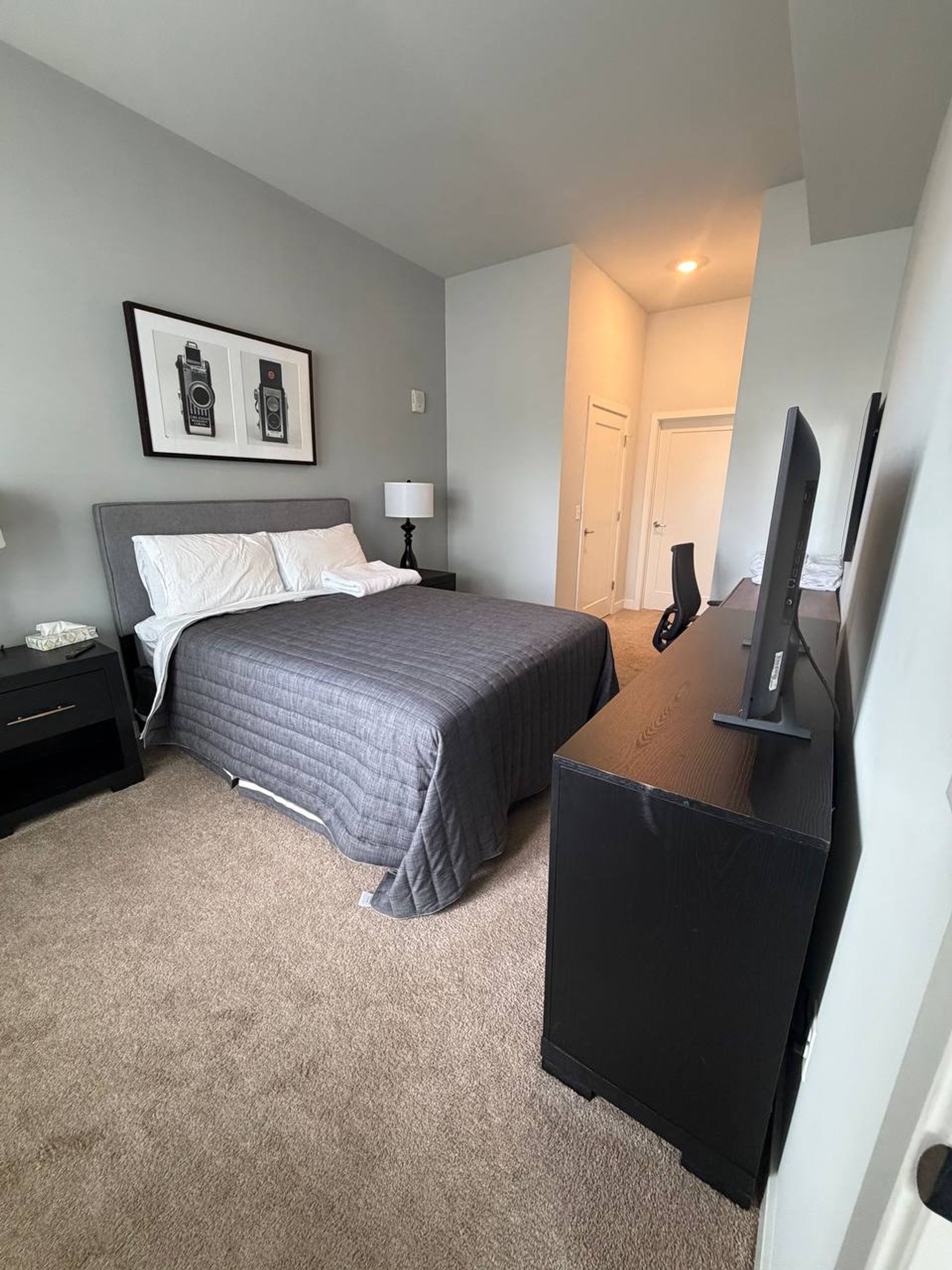 Bedroom with a made bed, folded towels and a dark dresser