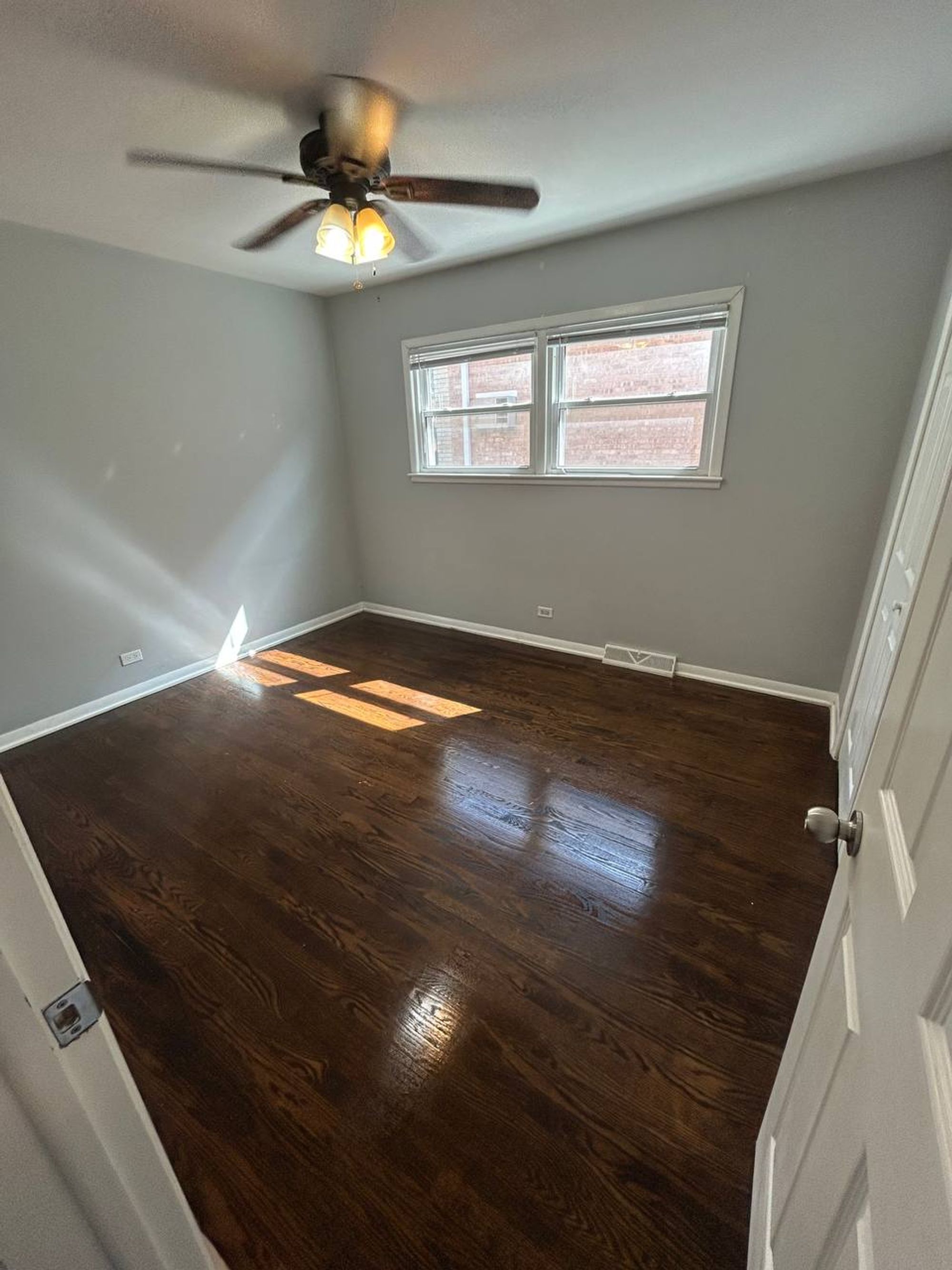 Empty bedroom with sunlight on freshly mopped dark wood floor