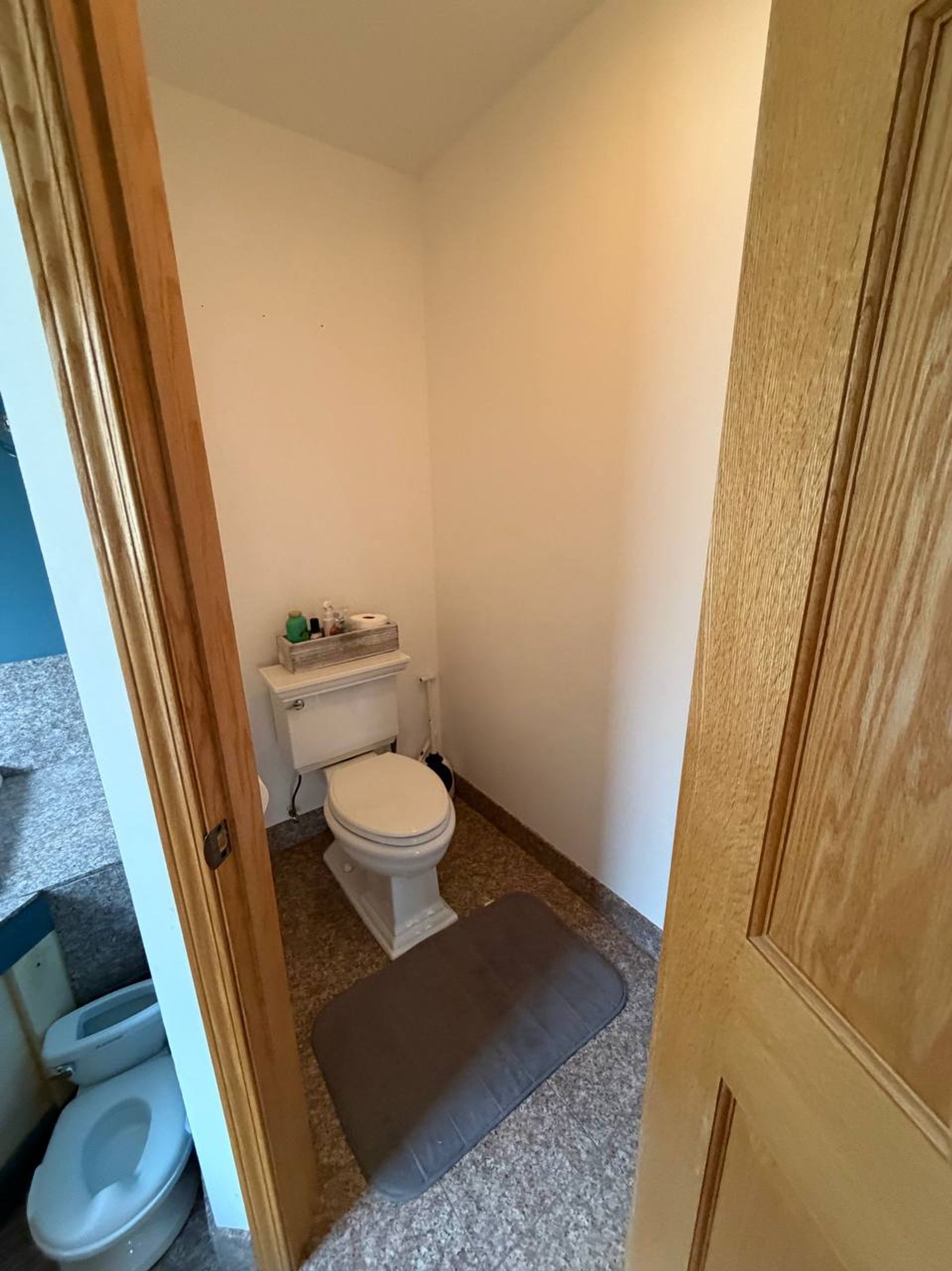 Small toilet room with a gray bath mat and stone tile floor